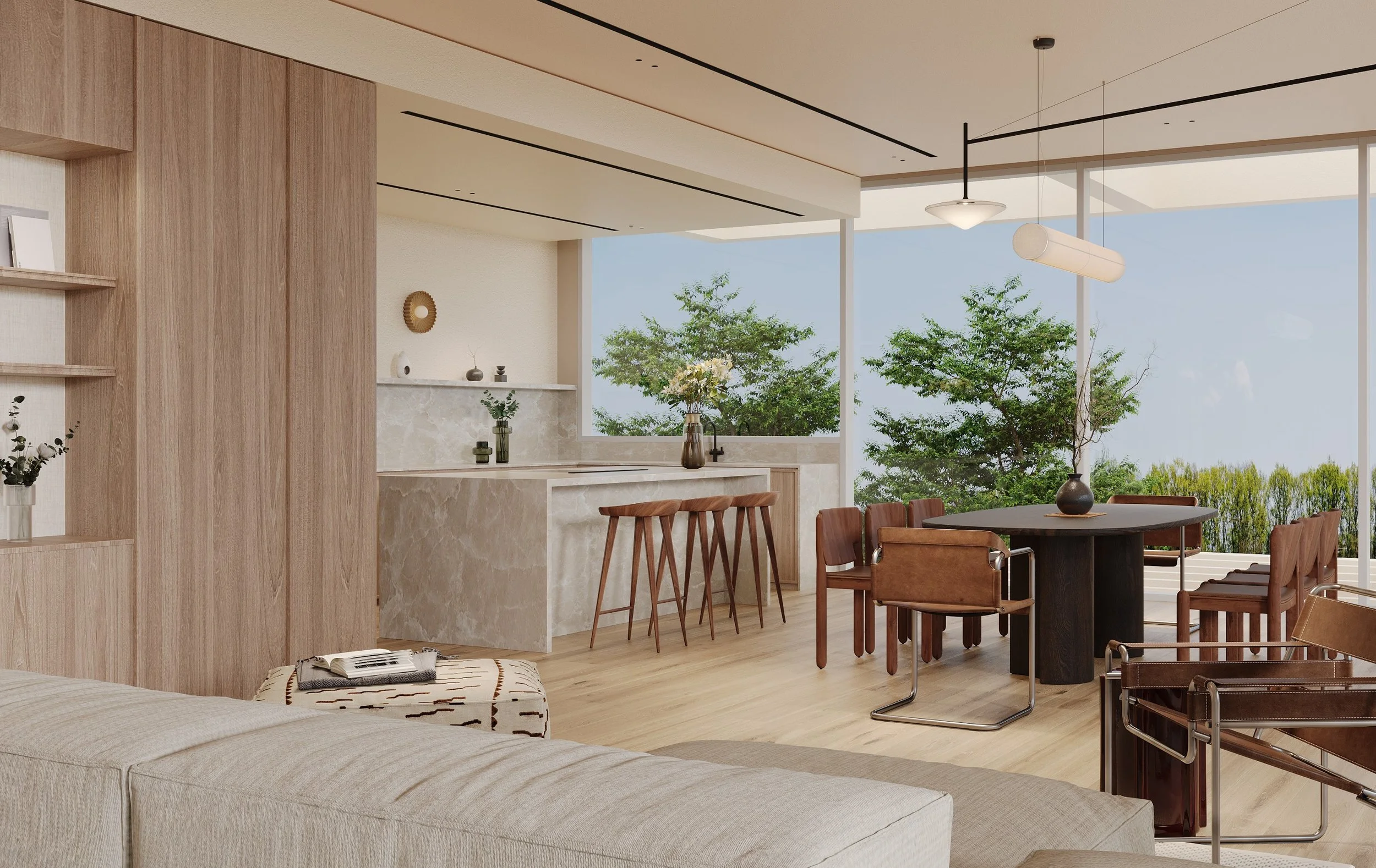 Modern living and dining area with large windows showing trees outside. There is a round black dining table with wooden chairs, a marble-topped kitchen island, and a beige sofa with a throw blanket and magazine. Decor includes vases and wall art.