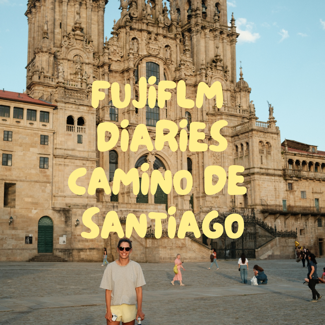 A smiling woman with sunglasses stands in front of a large historic cathedral during daytime with a clear blue sky, while other tourists are walking around.