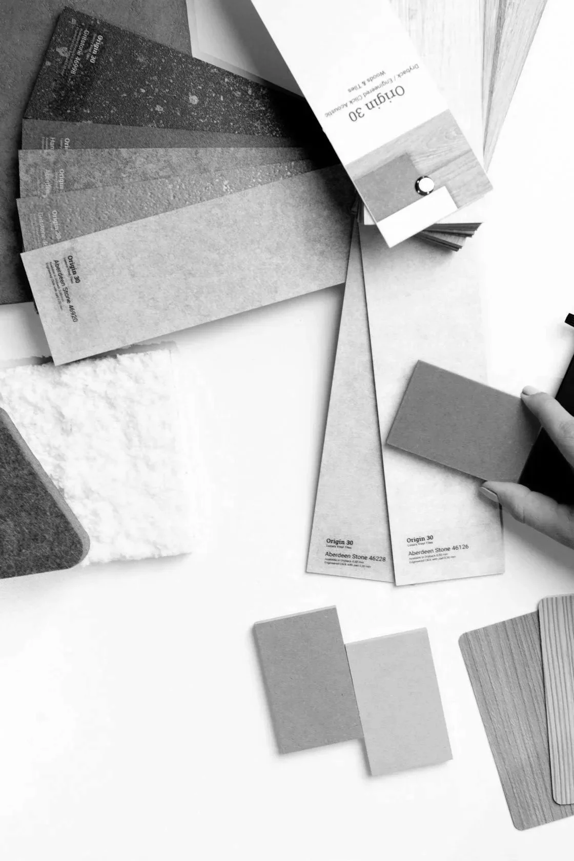 A person holds a small color sample card among various paint and material swatches, which are laid out on a flat surface. The scene appears to be a design or decorating project in progress.