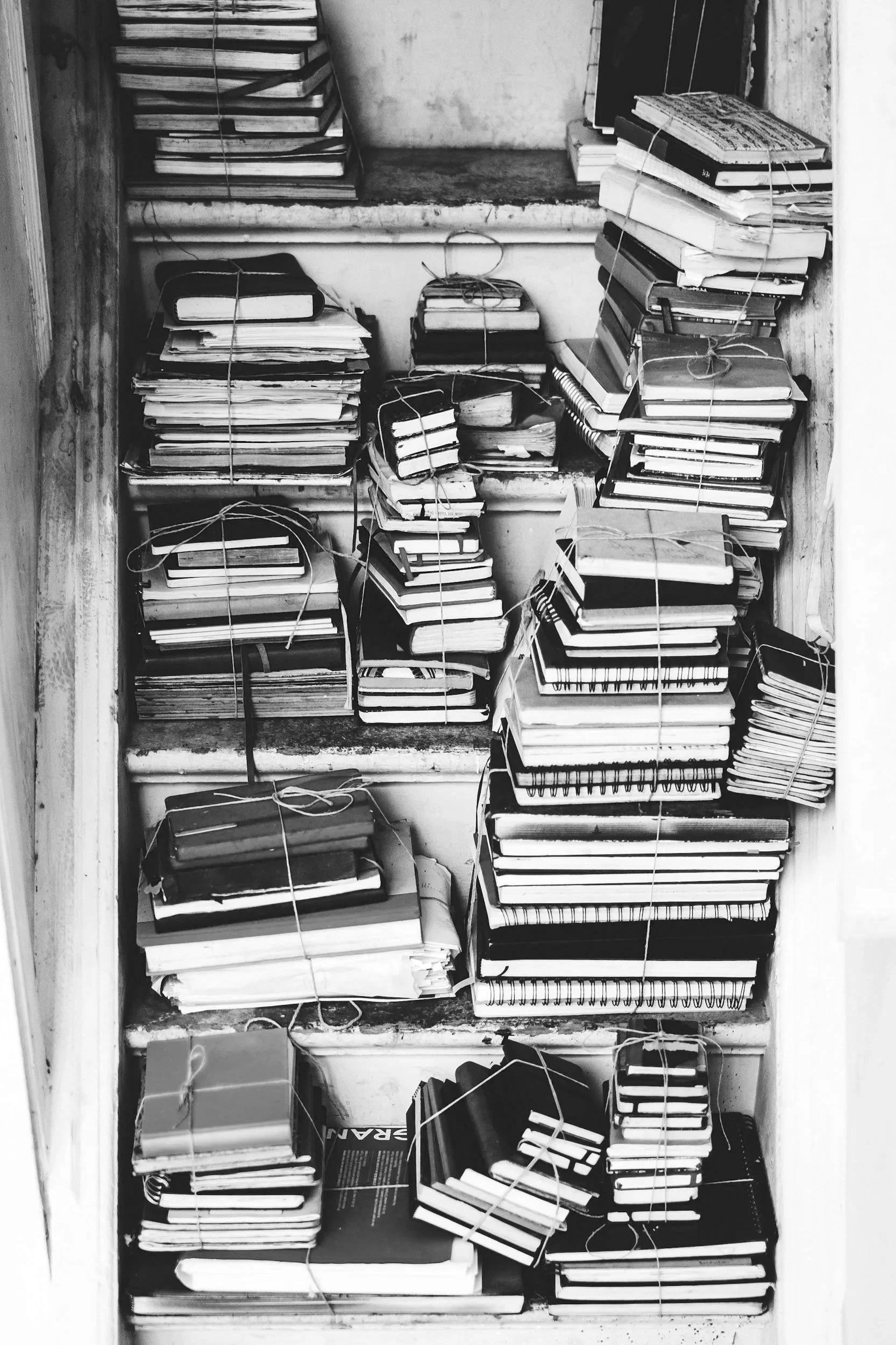 Several stacks of notebooks and papers are on shelves, tied with strings in a storage or attic space.
