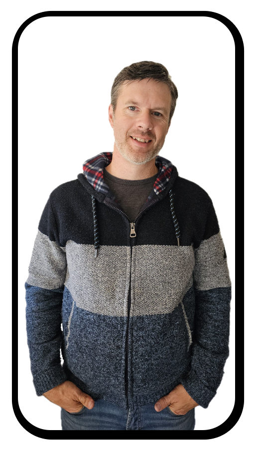 A man with short brown hair and a beard smiling at the camera, wearing a color-blocked zip-up sweater with a checkered hood.