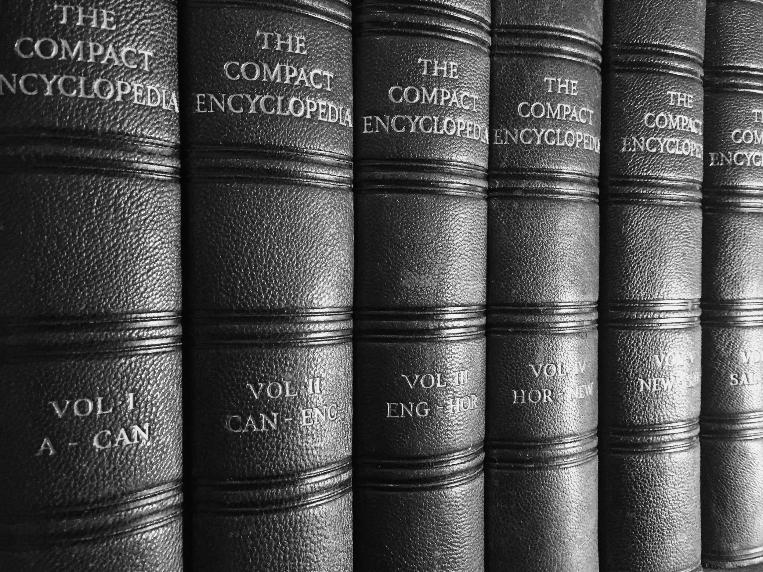 Une rangée de livres noirs de référence ou encyclopédies, avec des titres en relief, alignés côte à côte.