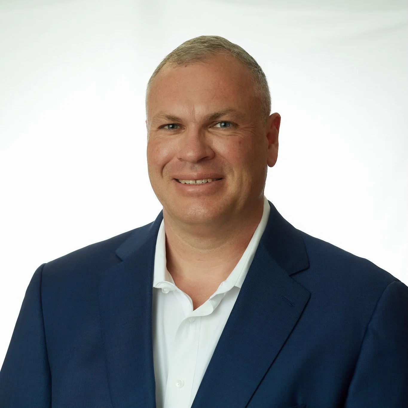 Headshot of Mark Peters in a navy blue suit with a white shirt, smiling against a plain white background.