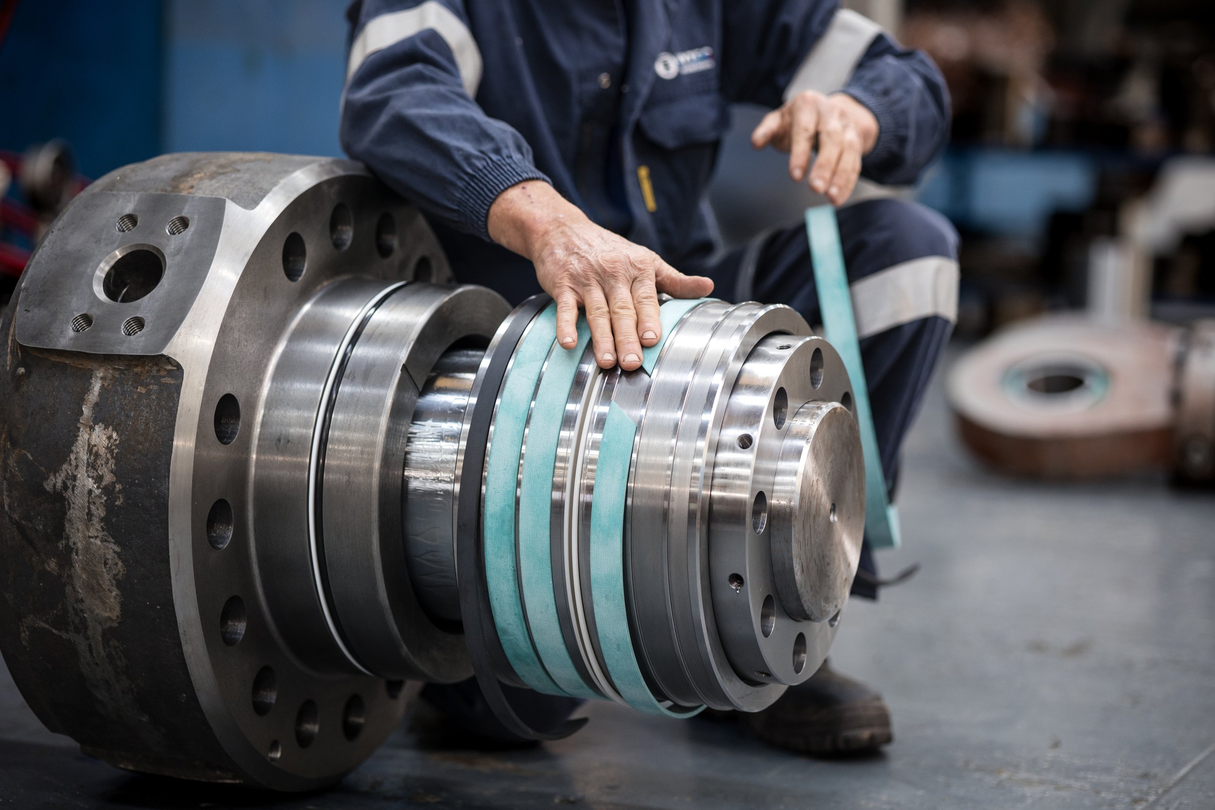 A worker's hands inspecting a large, partially assembled industrial machine component, possibly a bearing or a large gearbox, in a workshop setting.