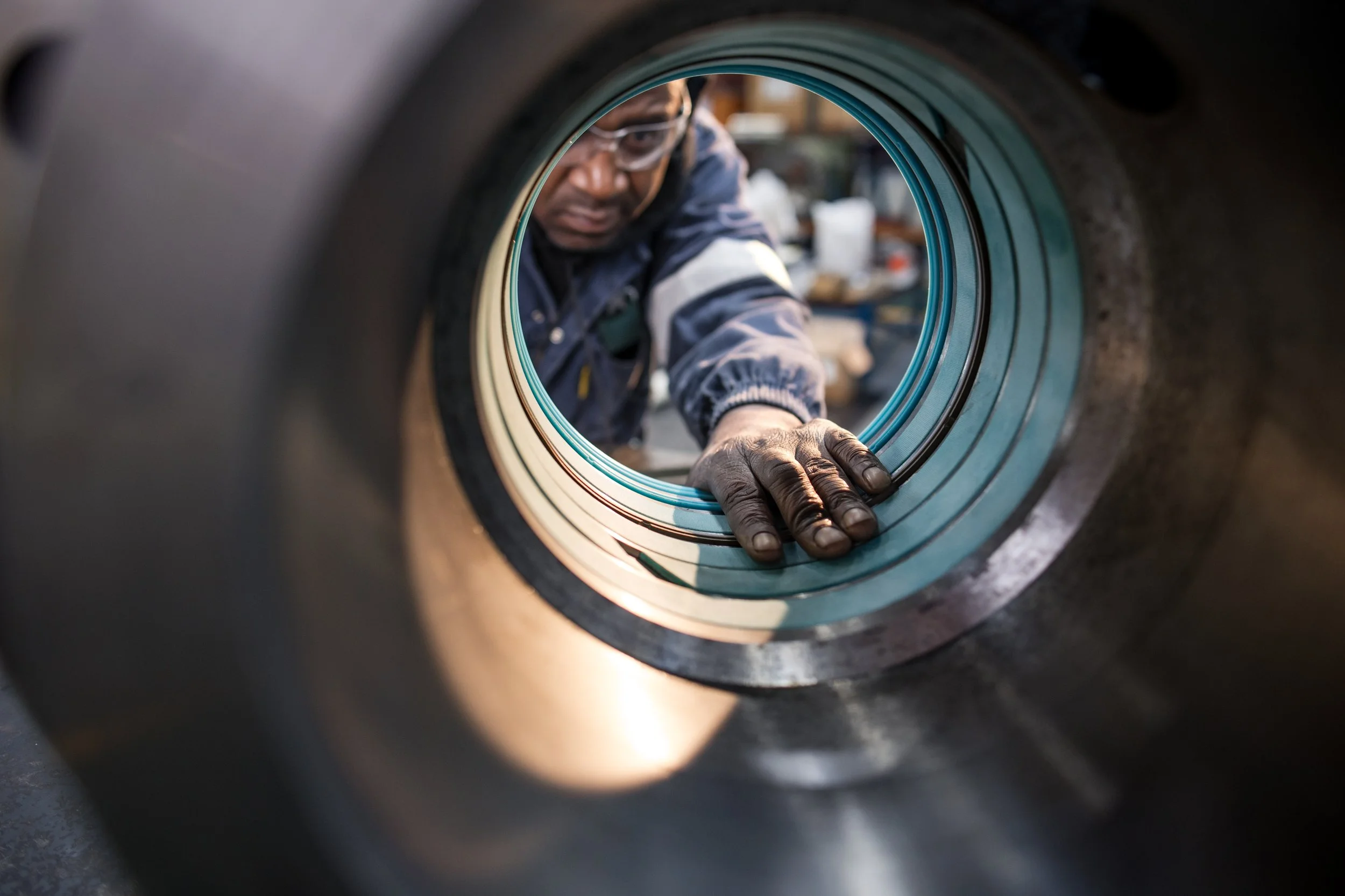 A person wearing safety glasses leans into a large industrial pipe or turbine, inspecting or working on its interior.