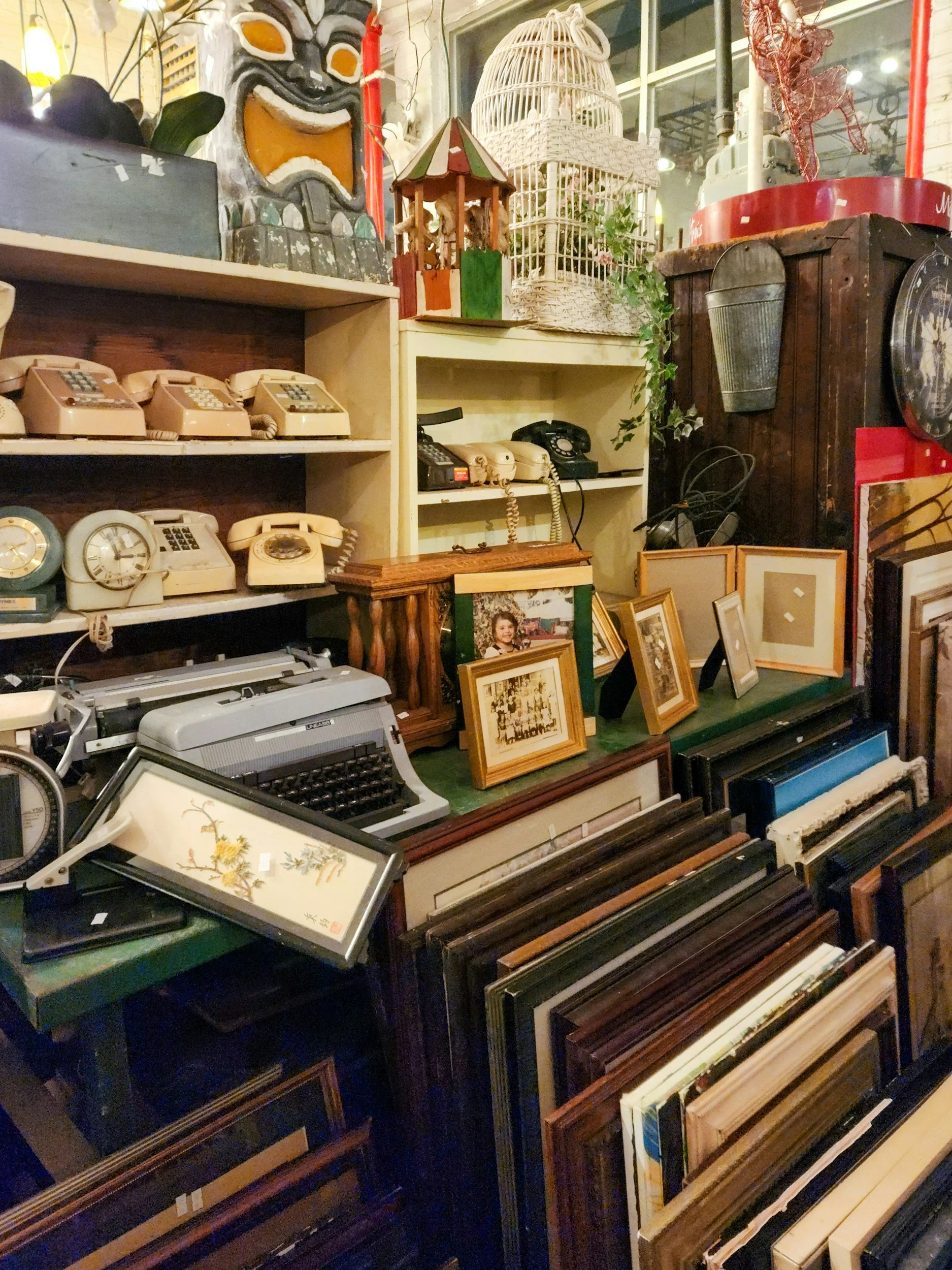 A collection of vintage items including old telephones, framed pictures, clocks, and artwork displayed on shelves in a store or antique shop.
