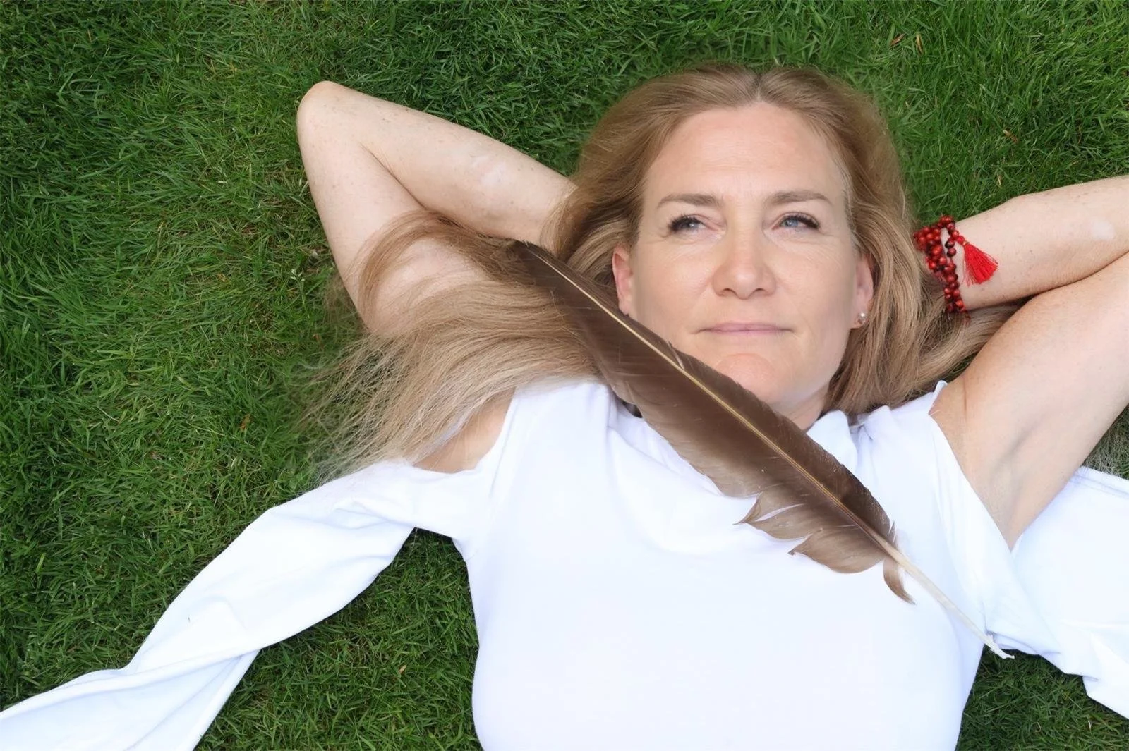 Stephanie Schneider Rittman of Aummagate laying in the grass with a hawk feather preparing for a healing session