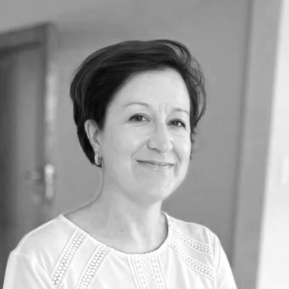 Black-and-white photo of a woman with short dark hair, smiling, wearing a light-colored top, standing indoors against a plain background.