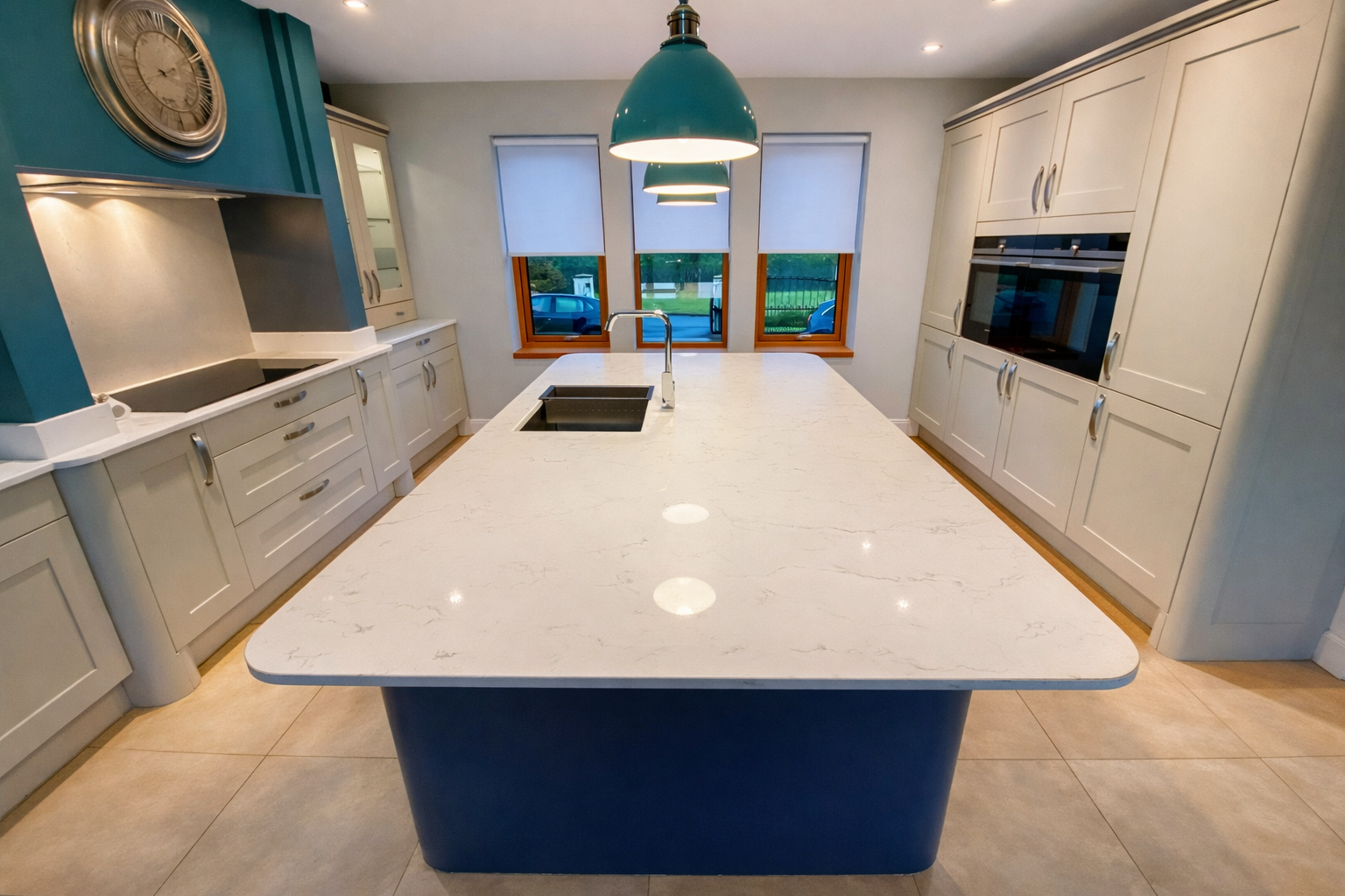 Modern kitchen with white cabinets, a large island with a white marble countertop, and three pendant lights hanging above. There are three windows on the back wall.