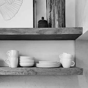 Weiße Kaffeetassen und -schalen auf einem Holzregal, im Hintergrund eine schwarze Gewürzdose und ein dekoratives Objekt.