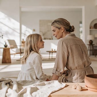 Eine Mutter und ein Kind sitzen einander im Wohnzimmer gegenüber und schauen sich liebevoll an