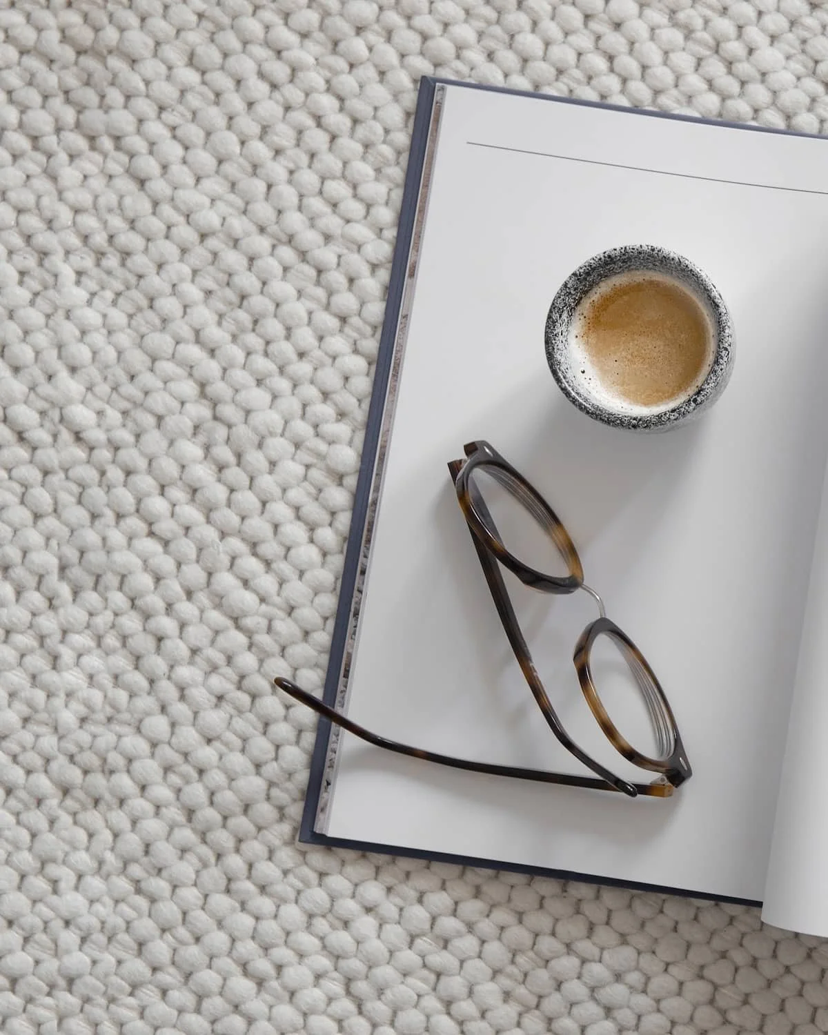 Ein kuscheliger Wollteppich, auf den ein Buch mit einer Brille liegen