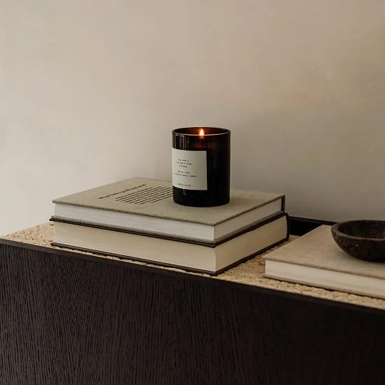 Ein dunkles Kerzenglas mit brennender Kerze auf zwei Büchern, und daneben eine kleine Schale