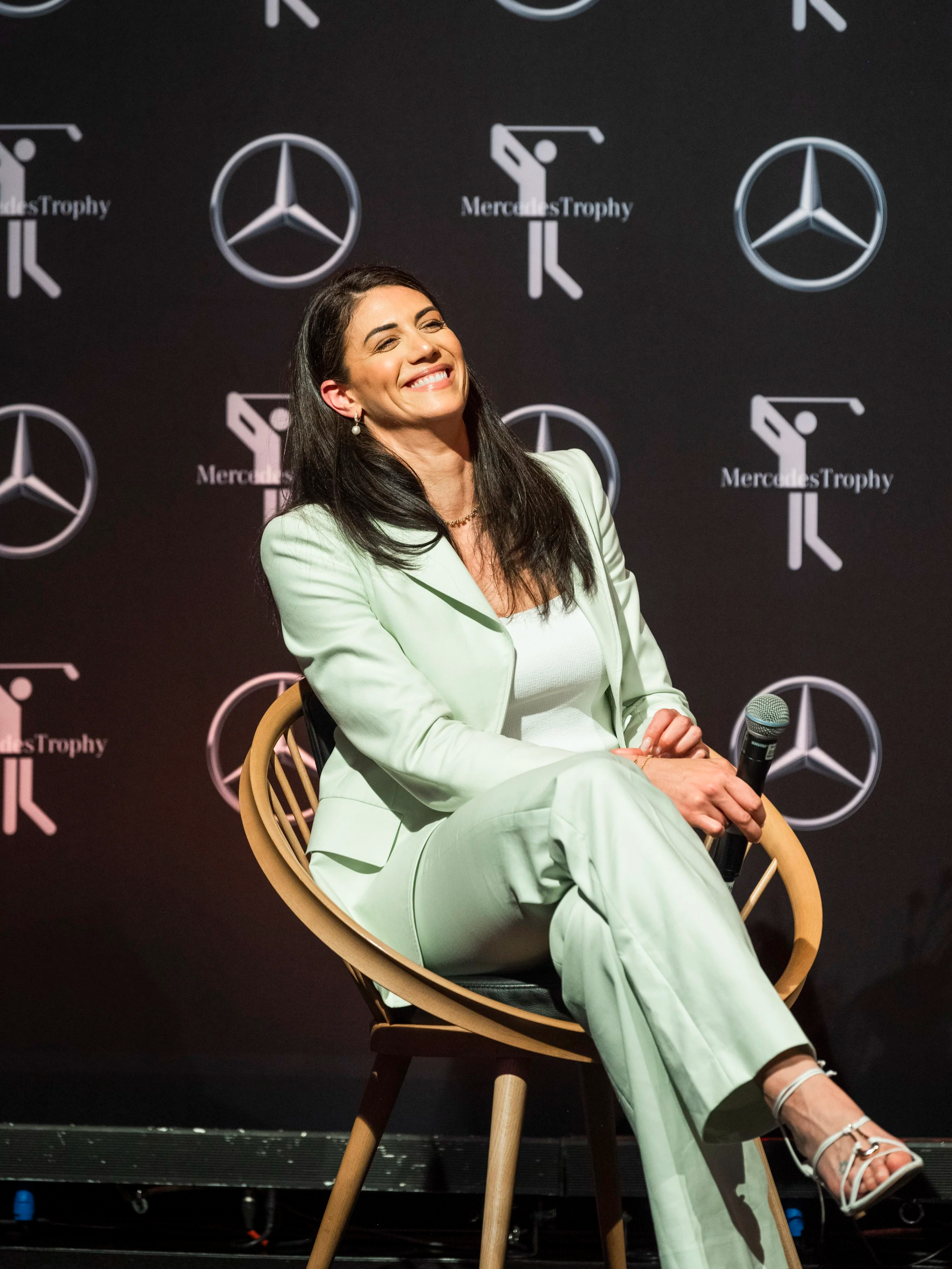 Stephanie Lassey (Rice) Olympic Champion keynote speaker at Mercedes-Benz MercedesTrophy event, seated holding microphone