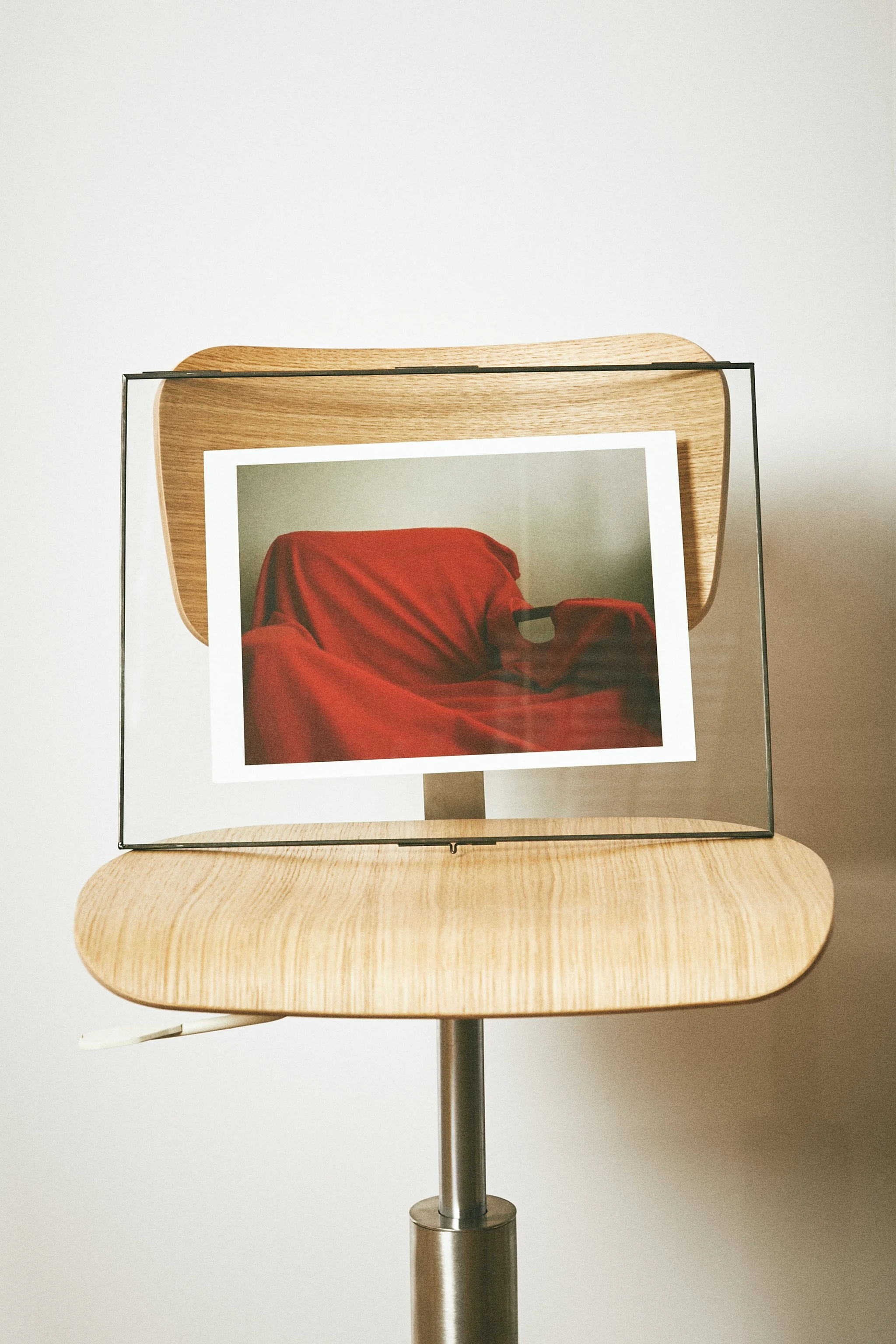 A wooden chair with a photo of a red draped fabric in a black frame resting on its backrest, set against a plain white background.