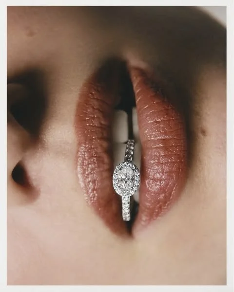 Close-up of lips with a lip ring holding a diamond engagement ring.