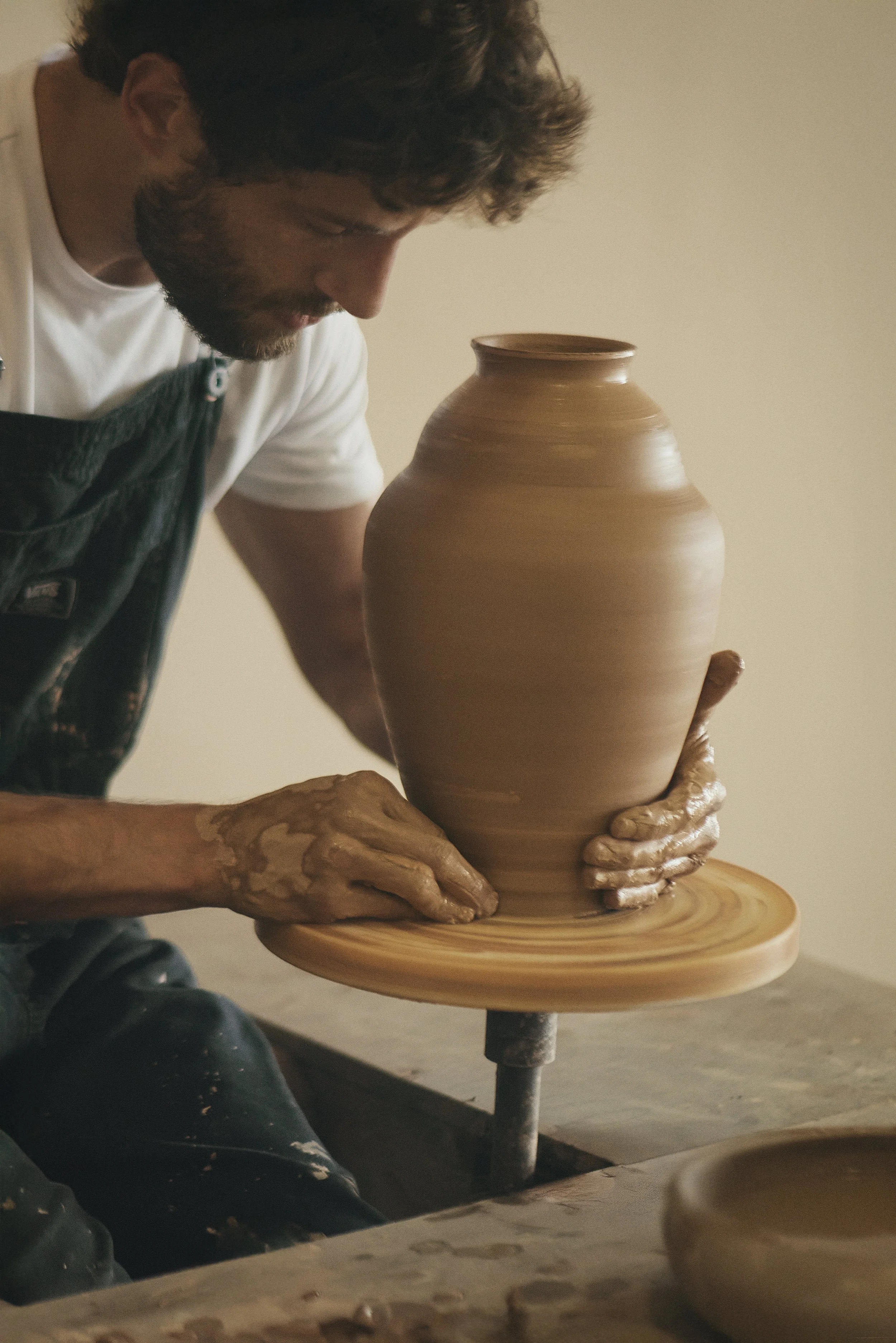 A person shaping a large clay vase on a pottery wheel.