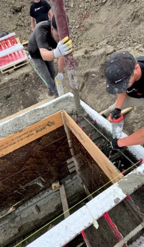 Workers pour concrete into a foundation framing at a construction site.