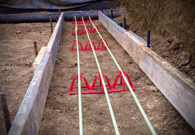 Construction site with wooden formwork and red runners for concrete pouring, with three white pipes in the center.