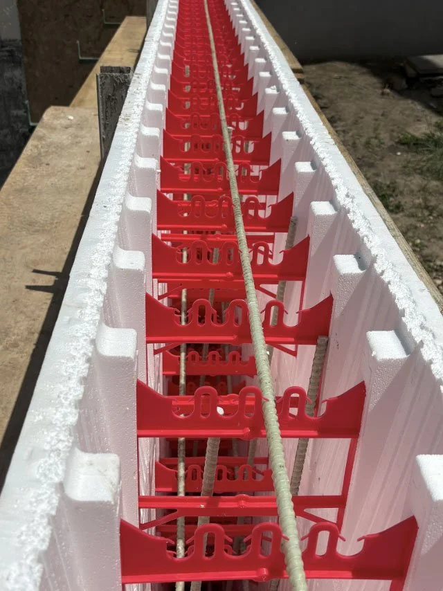 A long row of insulated foam panels with red plastic spacers and metal rebar rods inside as part of a construction process to form a concrete structure.
