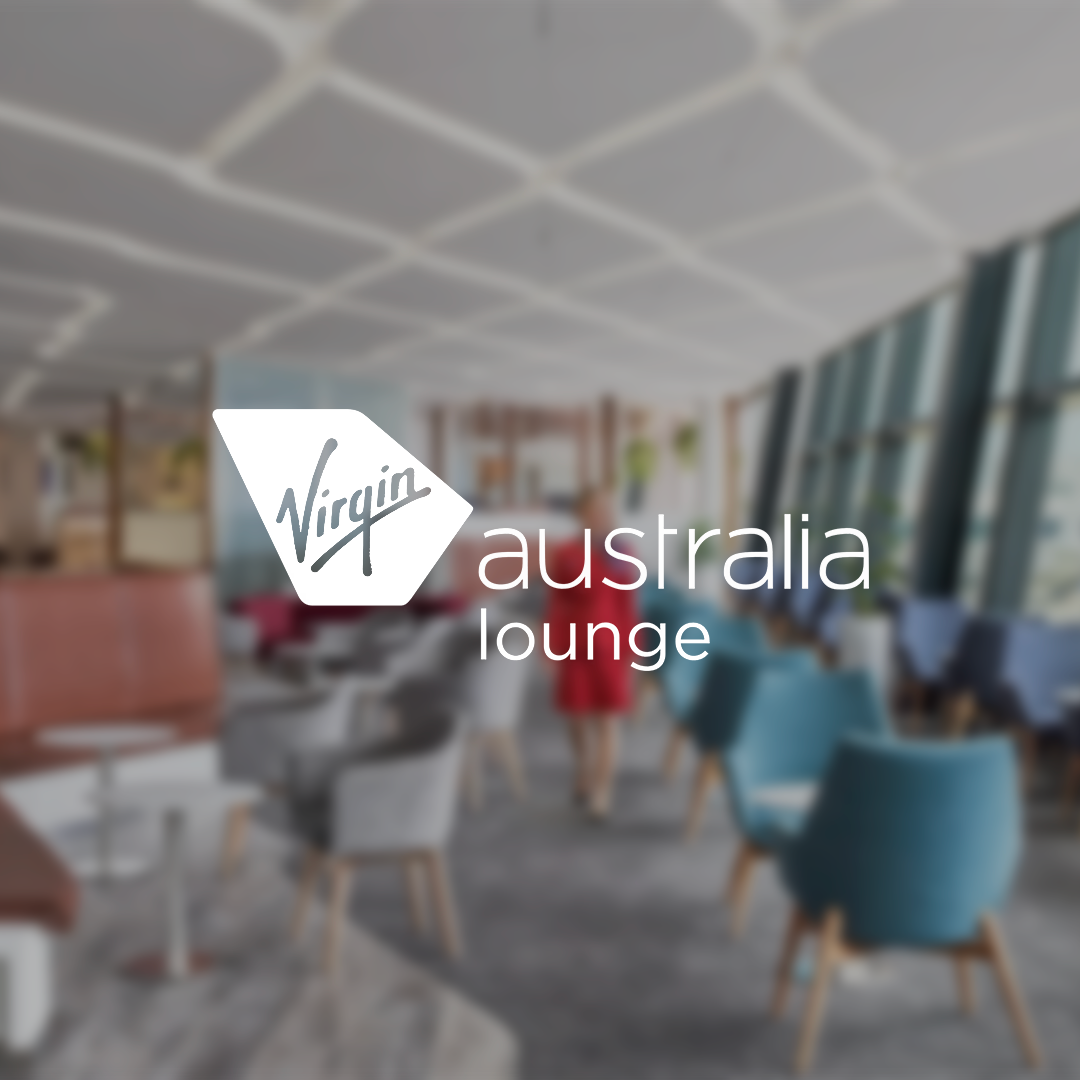 Interior of Virgin Australia lounge with chairs and a woman in a red dress walking in the background.
