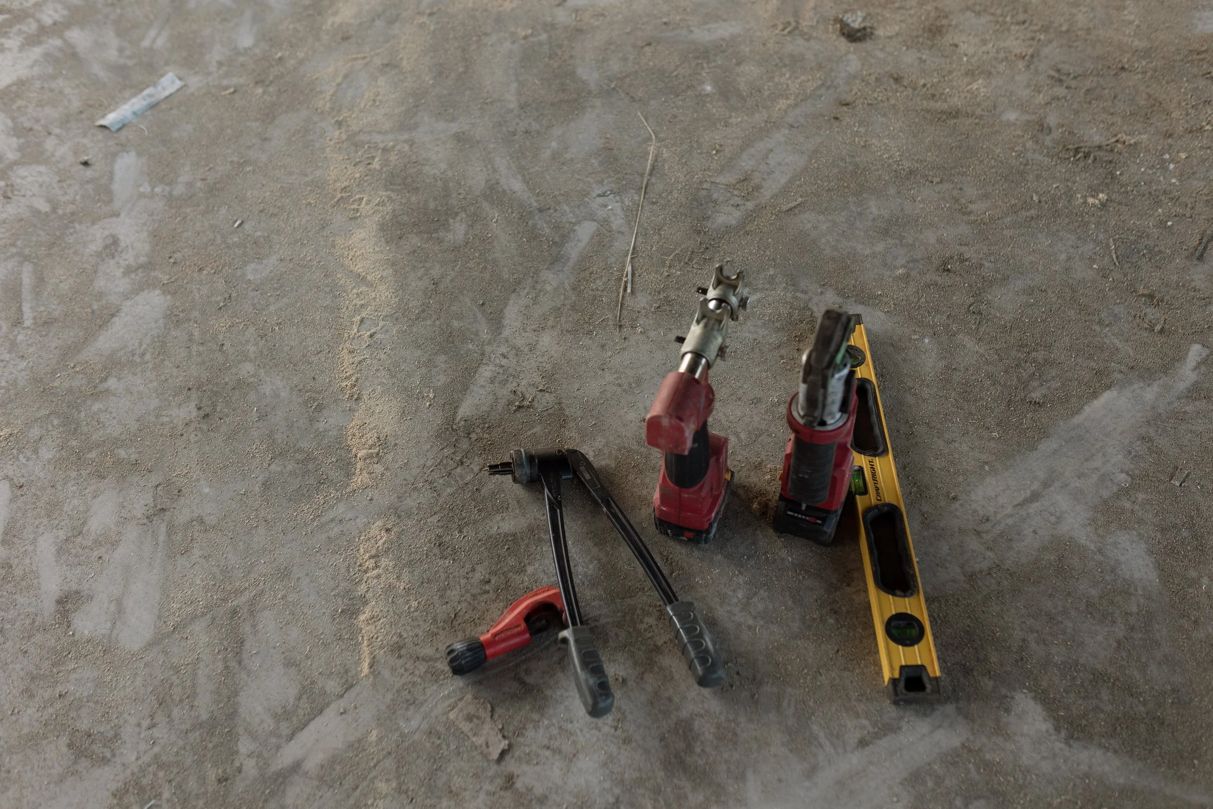 Construction tools including a cordless drill, a level, and a power saw placed on a rough concrete floor.