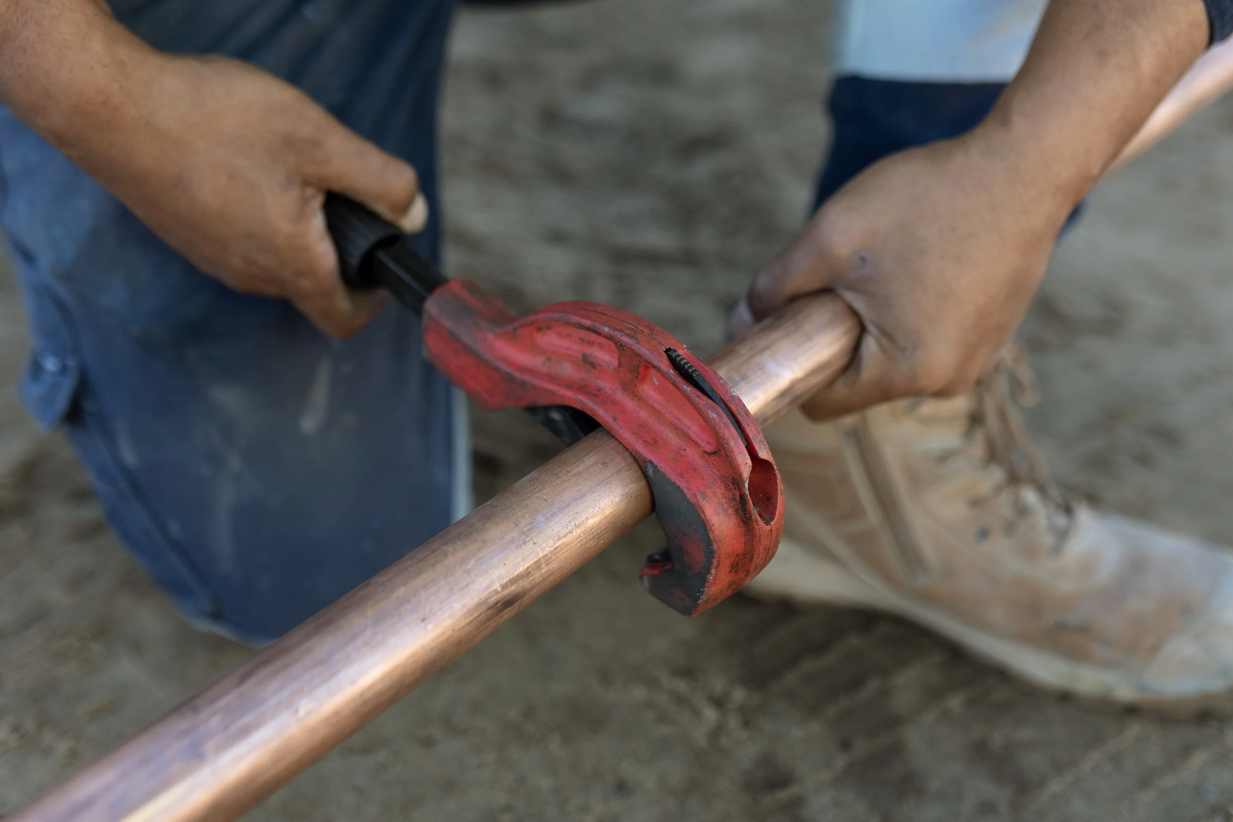 Close-up of hands securing a copper pipe using a red pipe clamp.