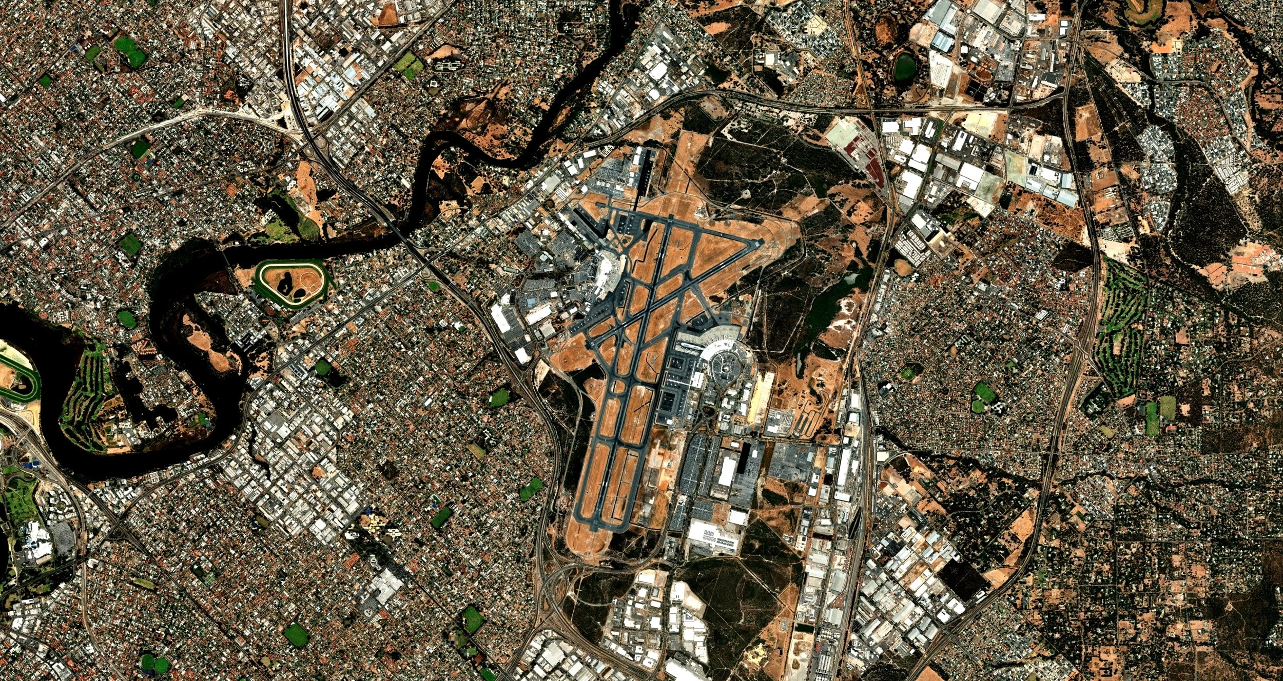 An aerial view of Perth, Western Australia, showing a major highway, an airport with runways, a river, and various residential, commercial, and industrial buildings.