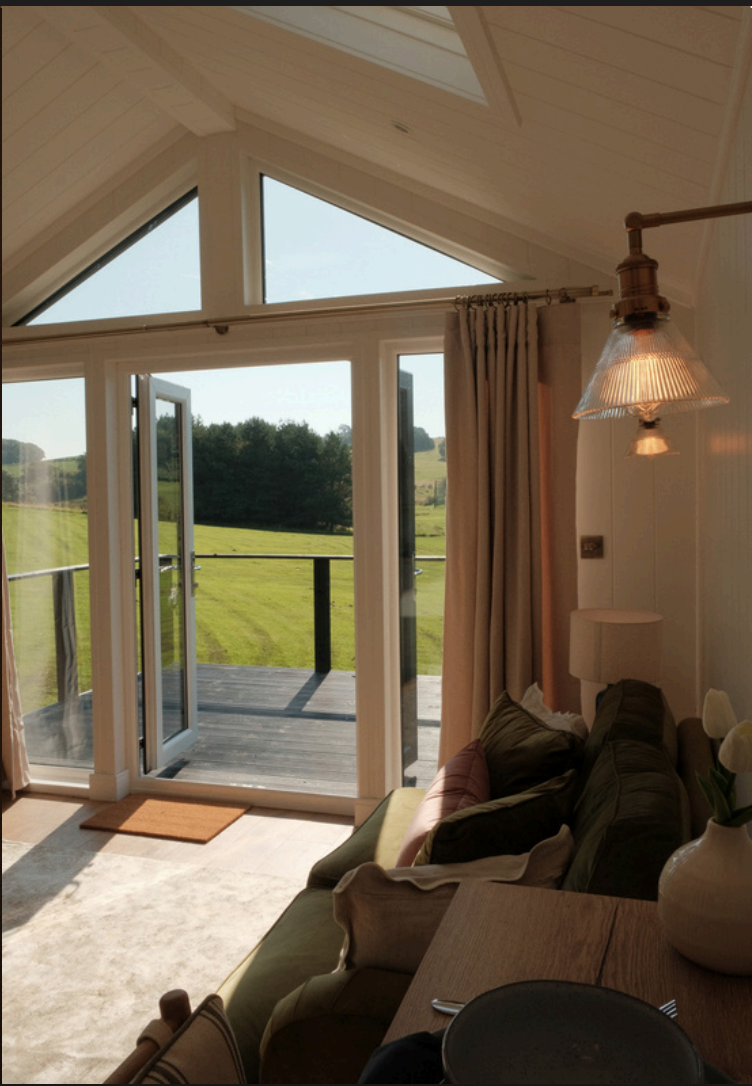Living room with large glass doors opening to a green outdoor landscape with a wooden deck.