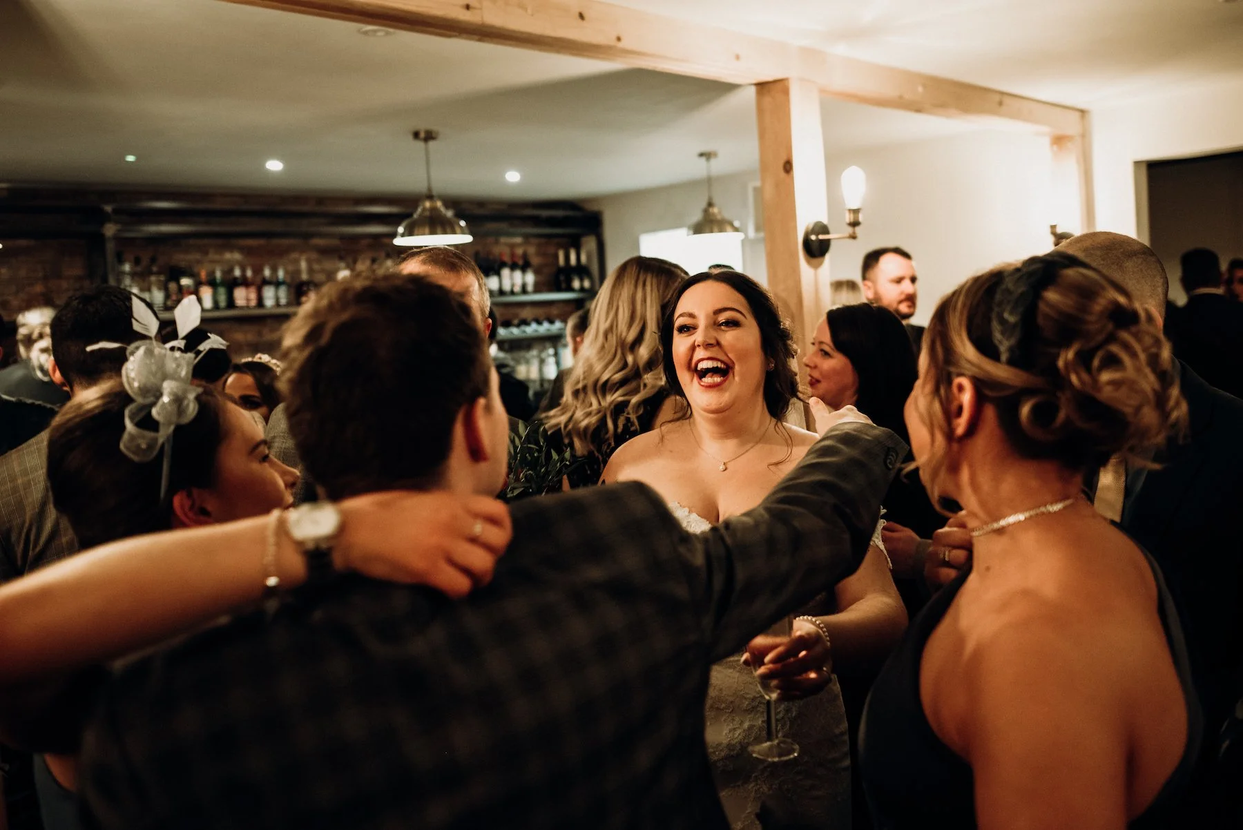 People celebrating at a social gathering, with a woman smiling and engaging in conversation among others in a warmly lit indoor setting.