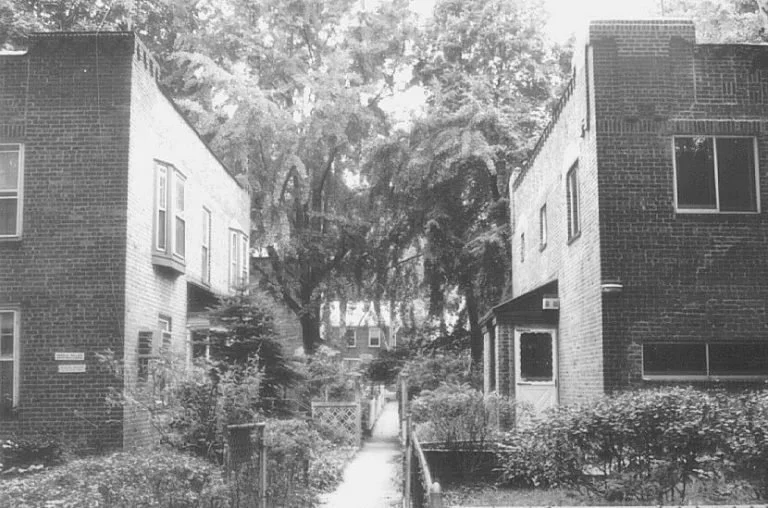 Historic black-and-white view of a pedestrian path between brick row houses in Sunnyside Gardens