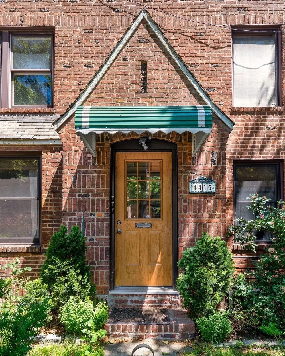 Brick Sunnyside Gardens row house with a gabled entrance, wood door and planted front garden
