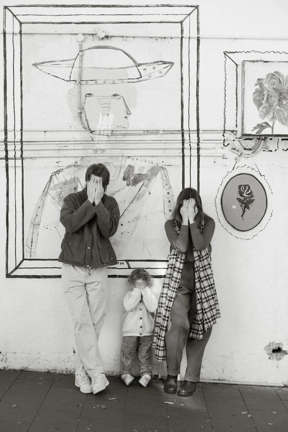 A playful family portrait in front of a wall of artwork, in black and white.
