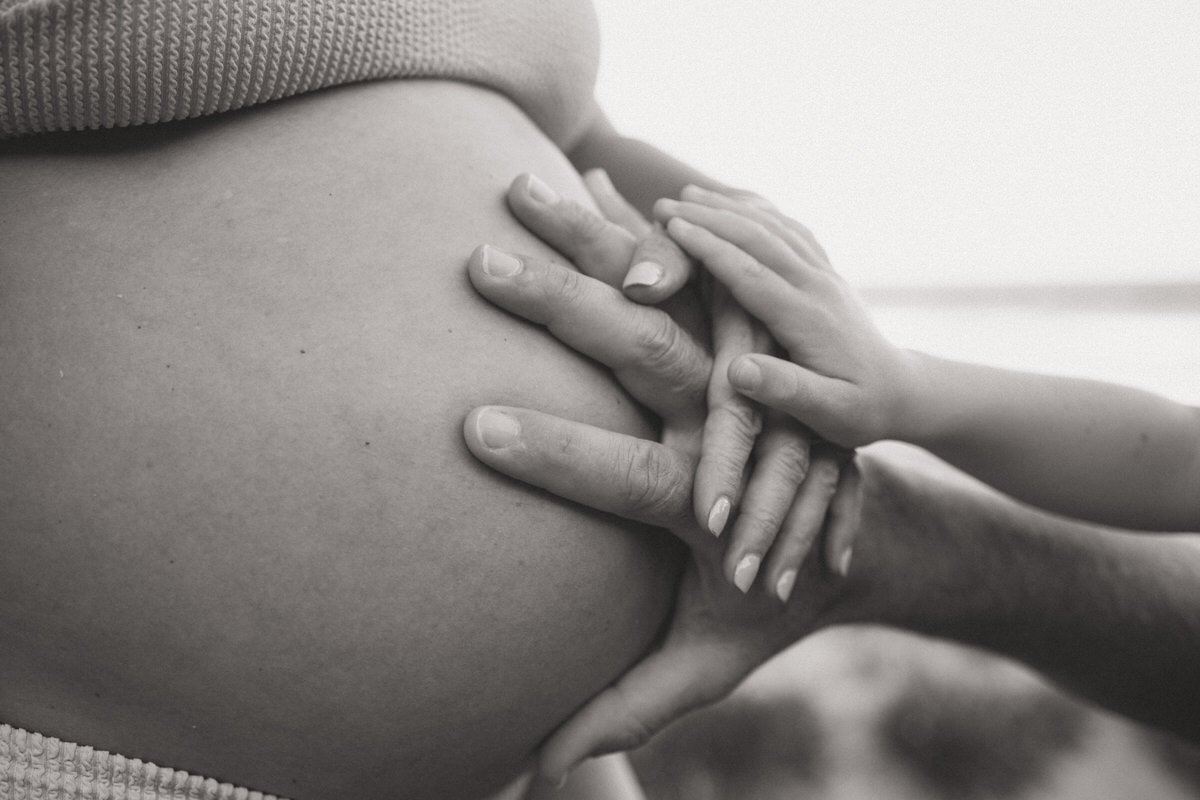 Close-up of a person gently holding their pregnant belly with two hands.
