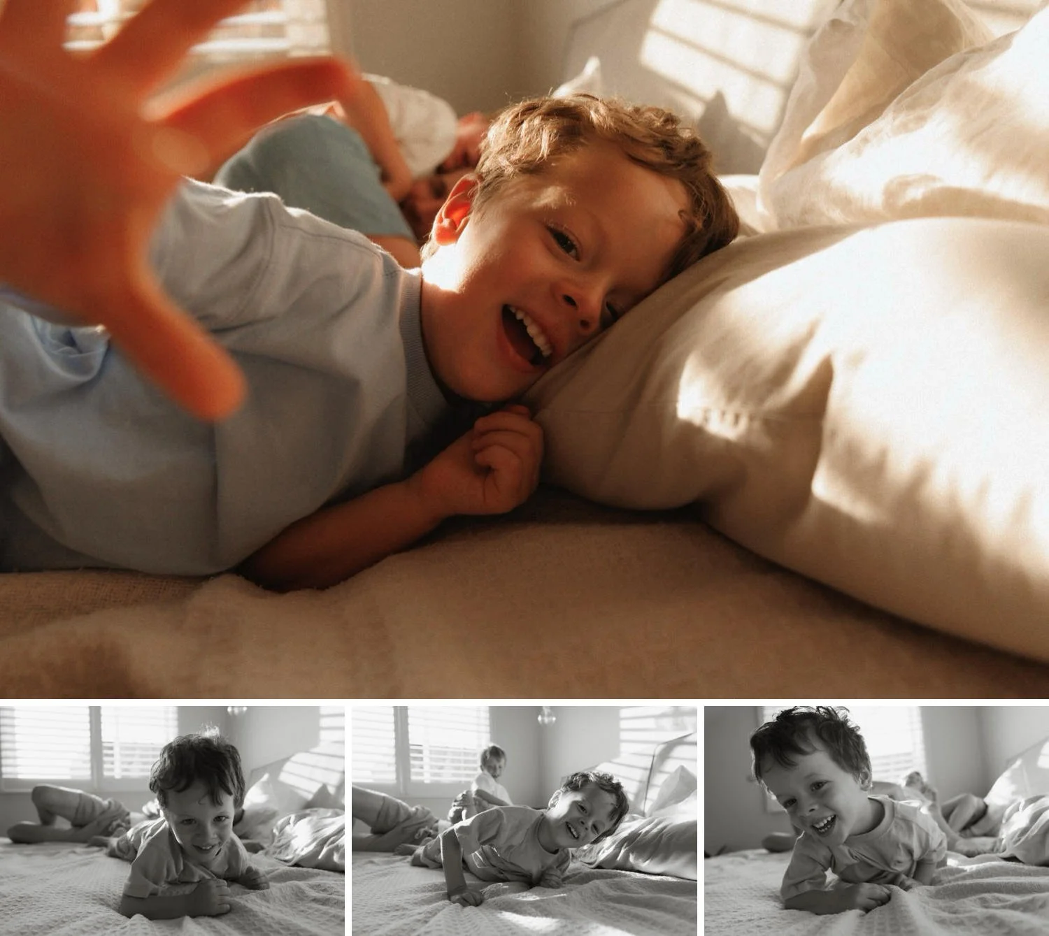 Little boy smiling and reaching toward the camera while playing on the bed in soft natural light.