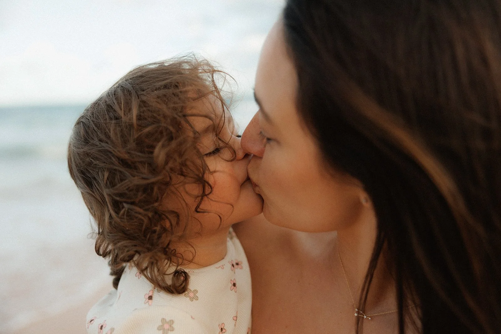 Mother and toddler daughter kissing on beach