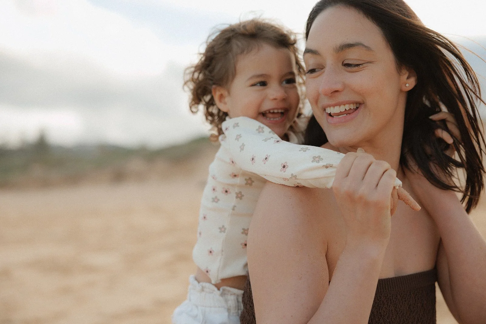 Mother piggybacking toddler daughter on beach