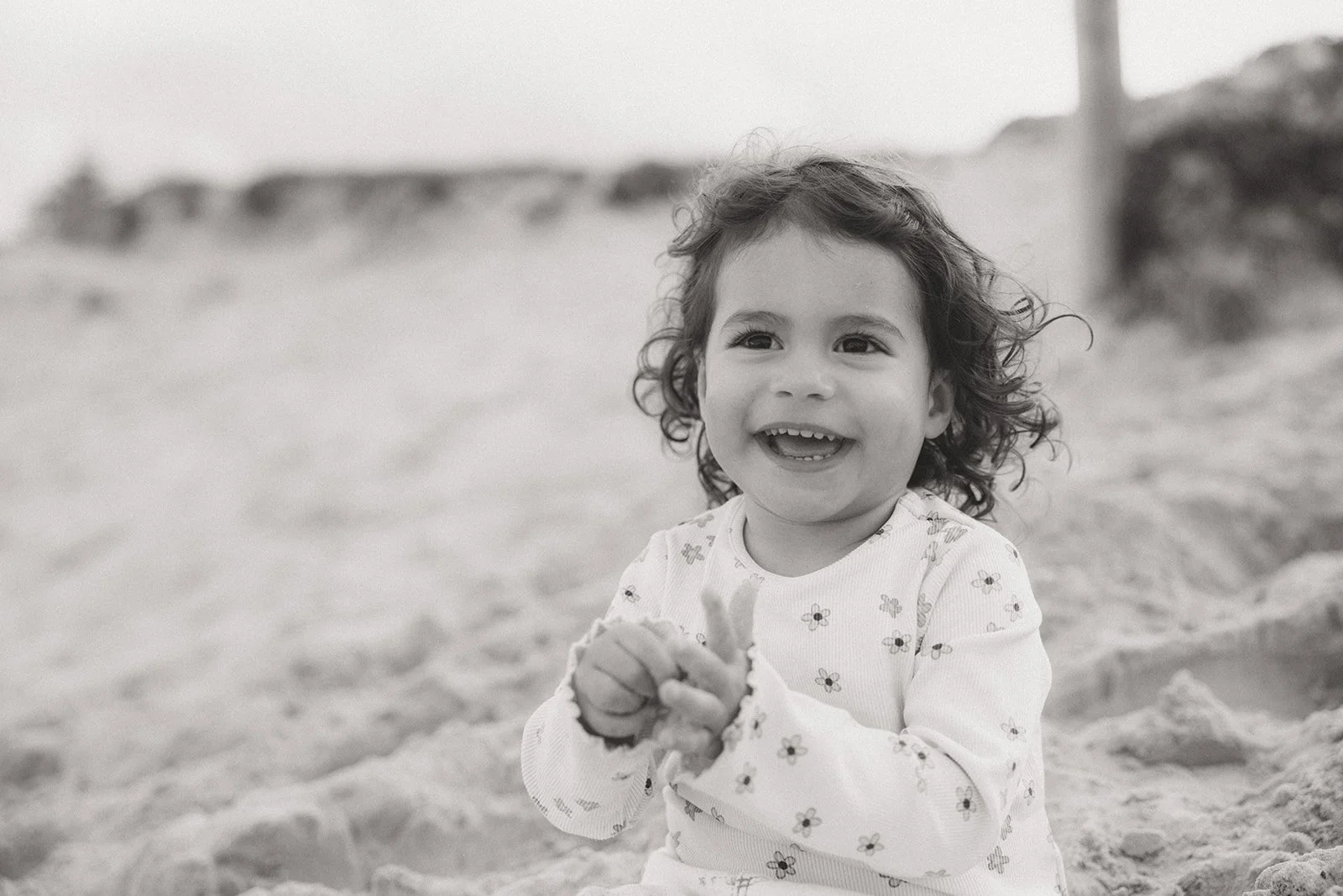 Toddler girl smiling, sitting on beach
