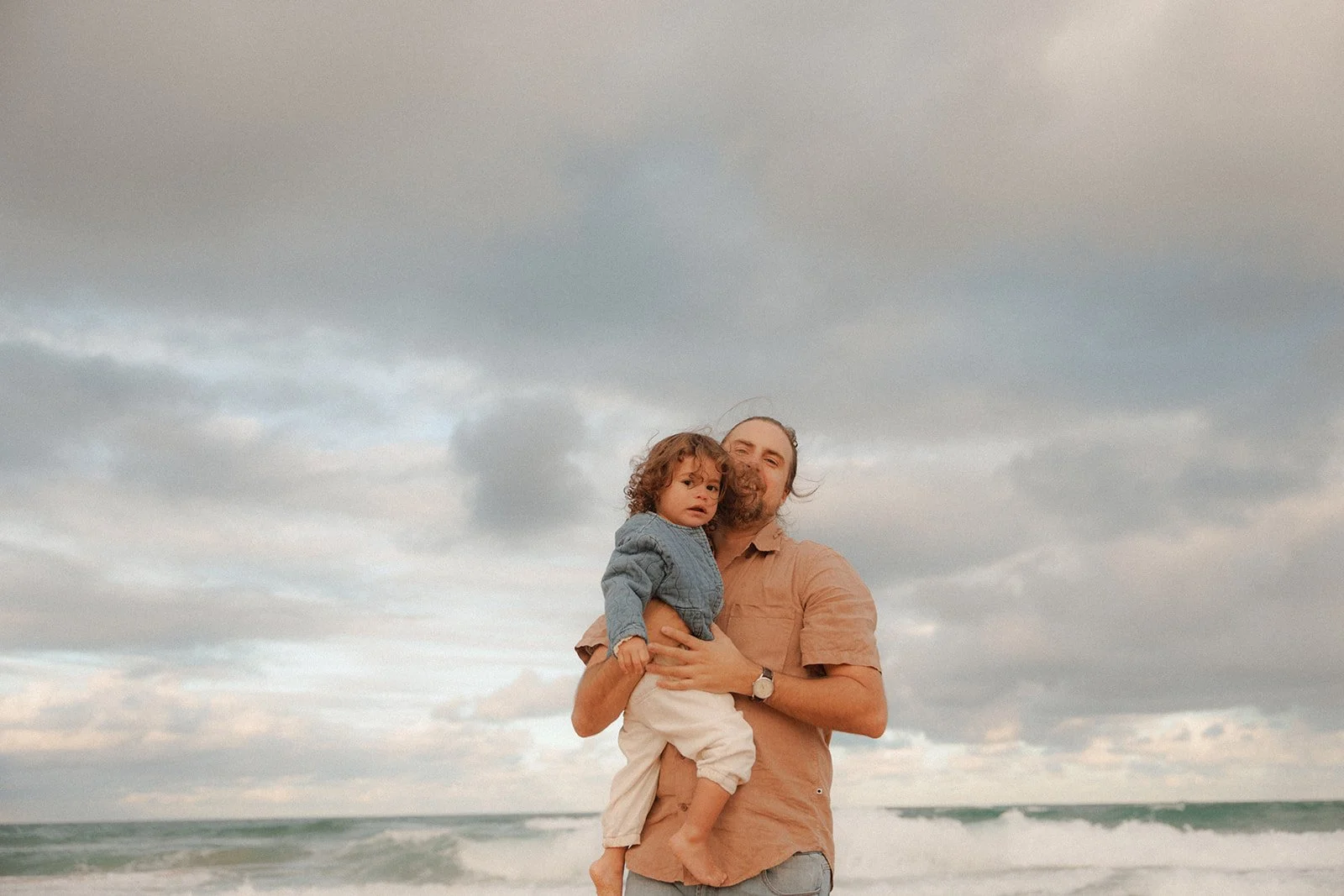 Father with toddler daughter with rough sea and cloudy sky behind
