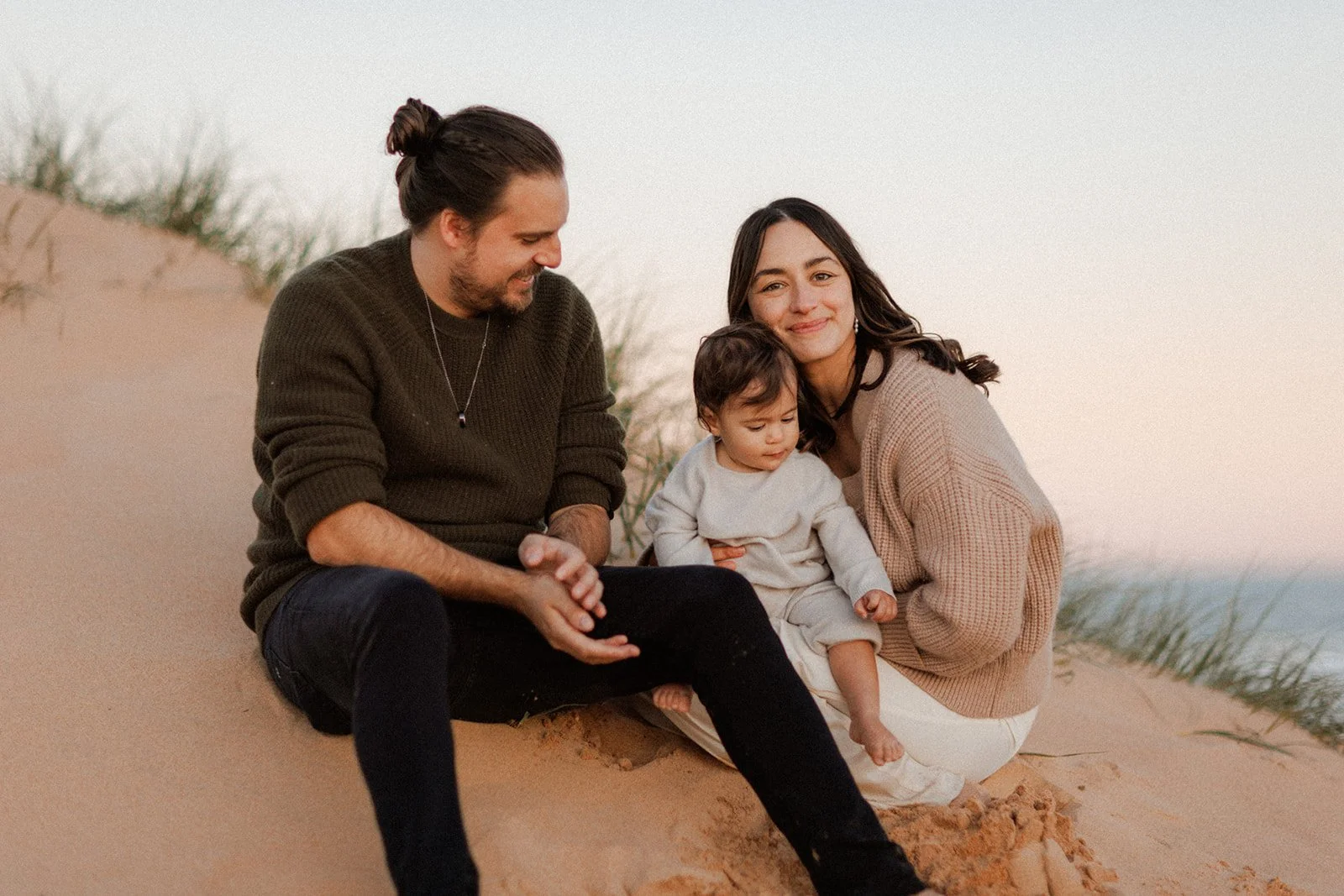 Mother and father with baby girl, sitting together on sand dune