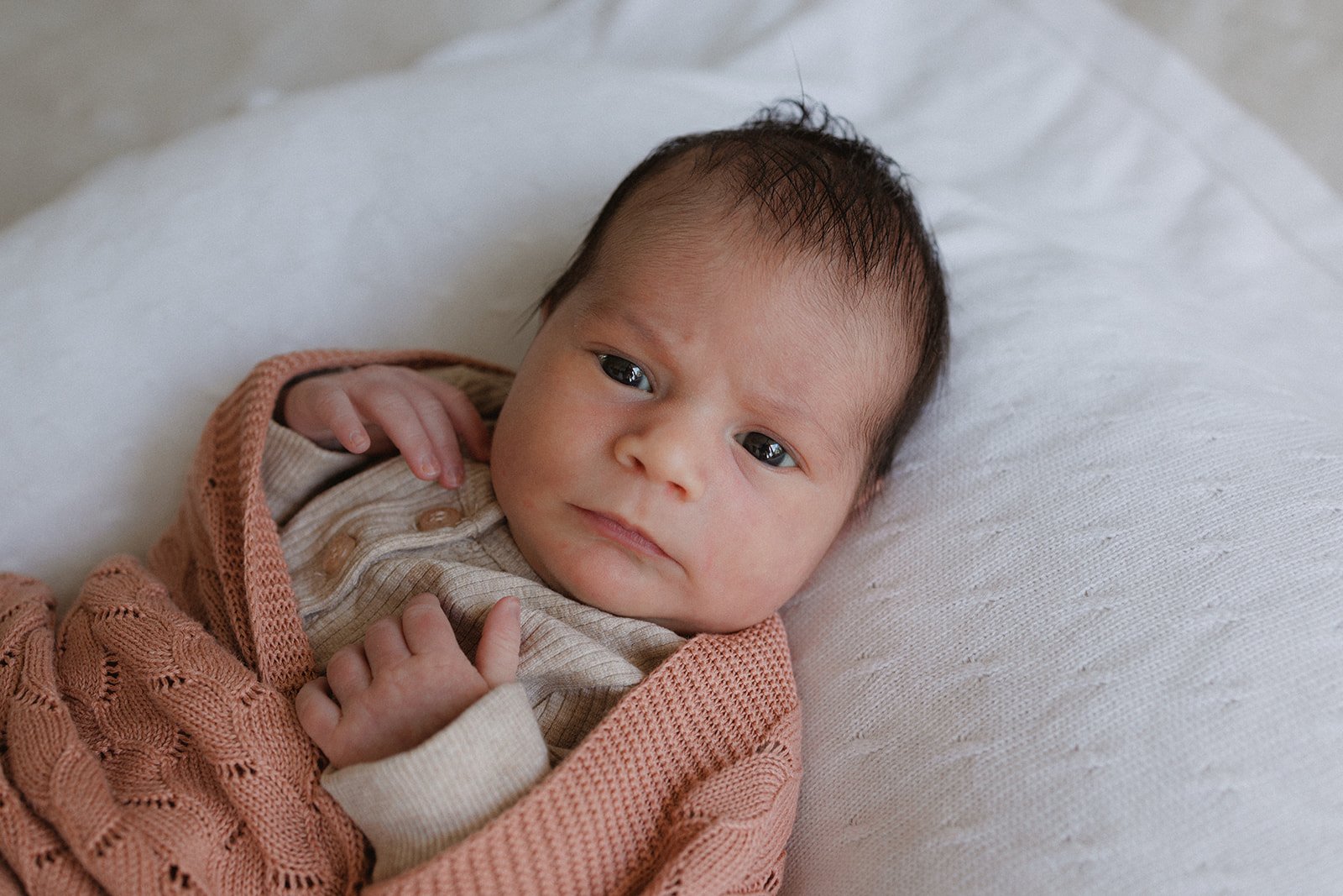 Baby wrapped in pink blanket lying on bed