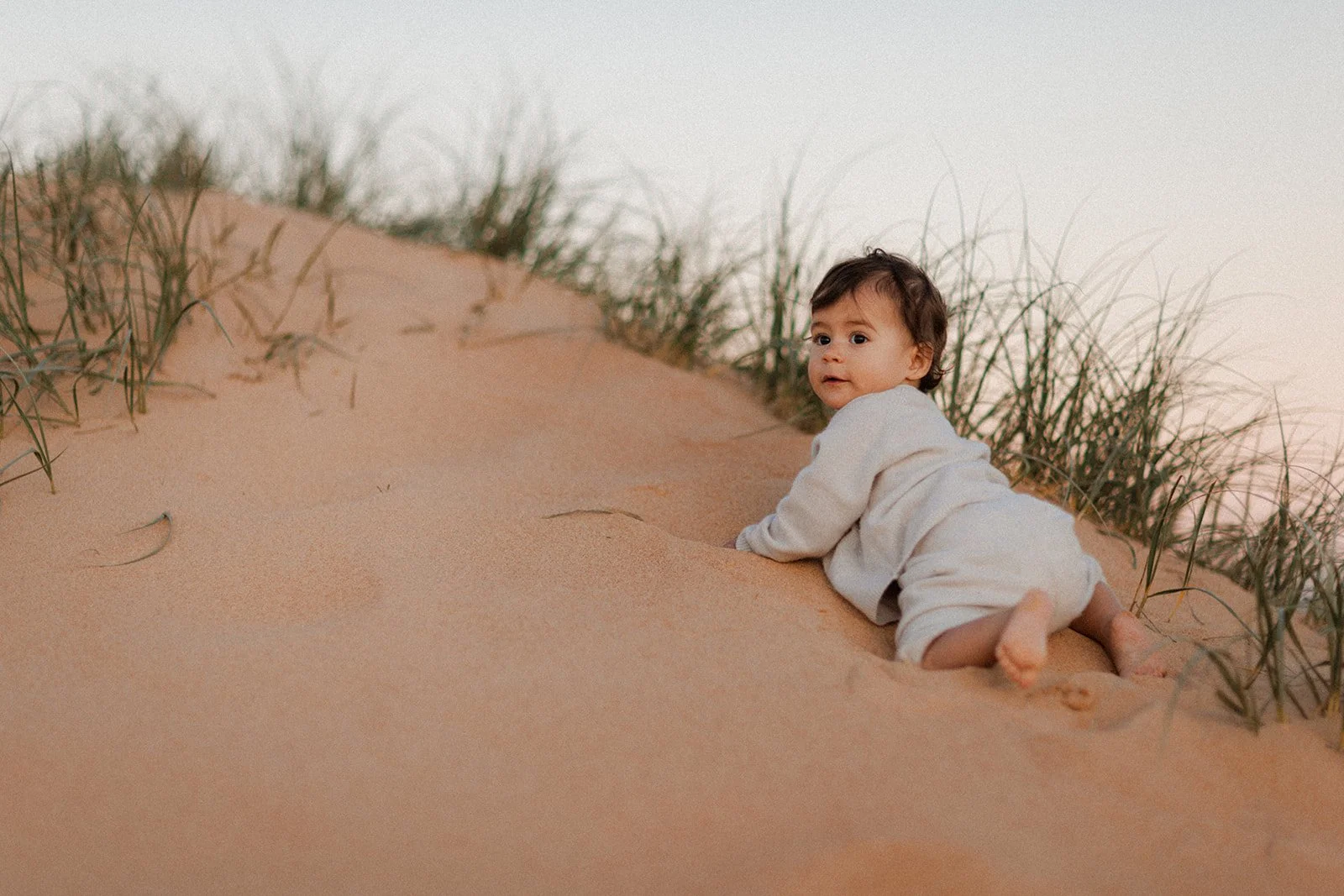 Baby girl in cute outfit climbing on sand dune