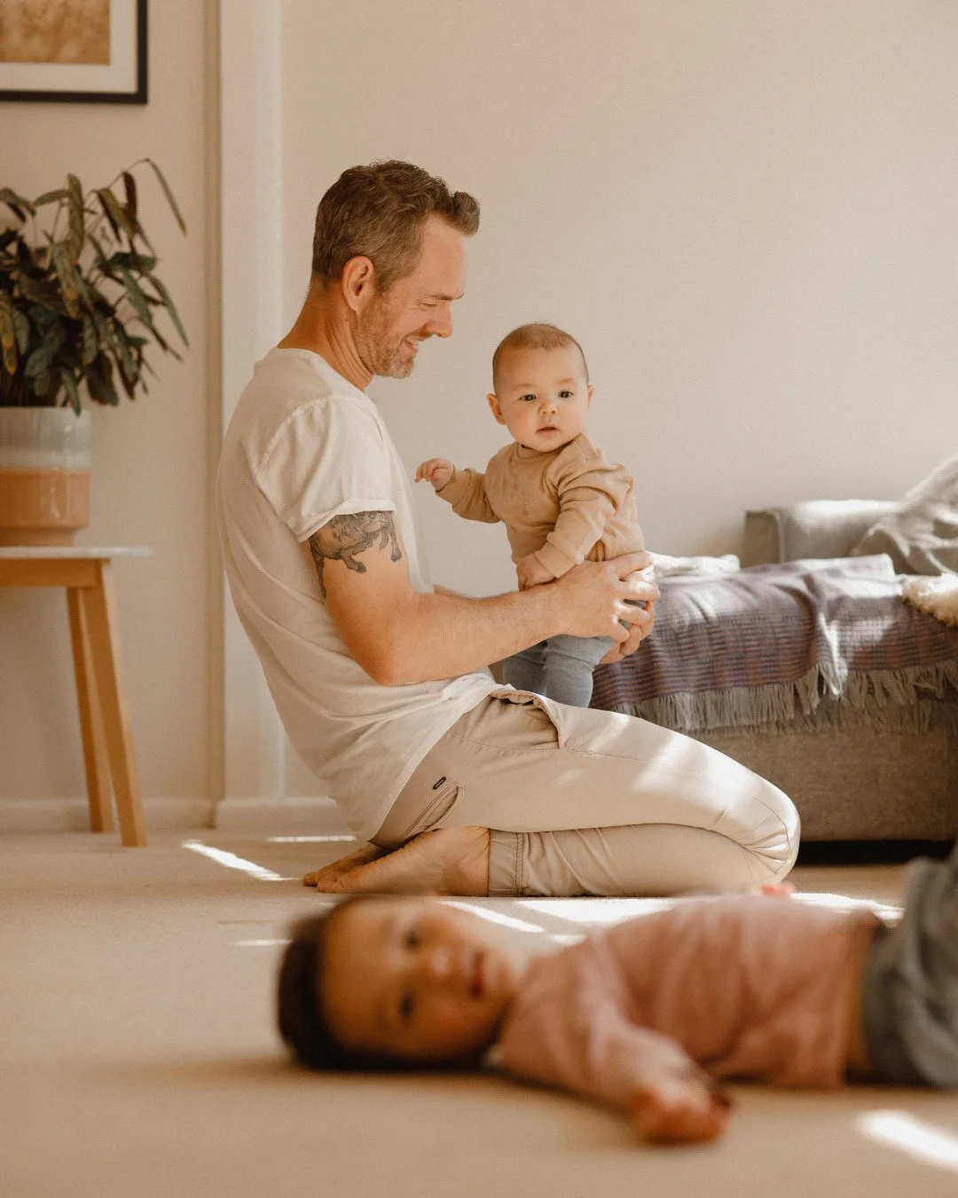 Father sitting on the floor holding newborn baby, with toddler lying on the floor
