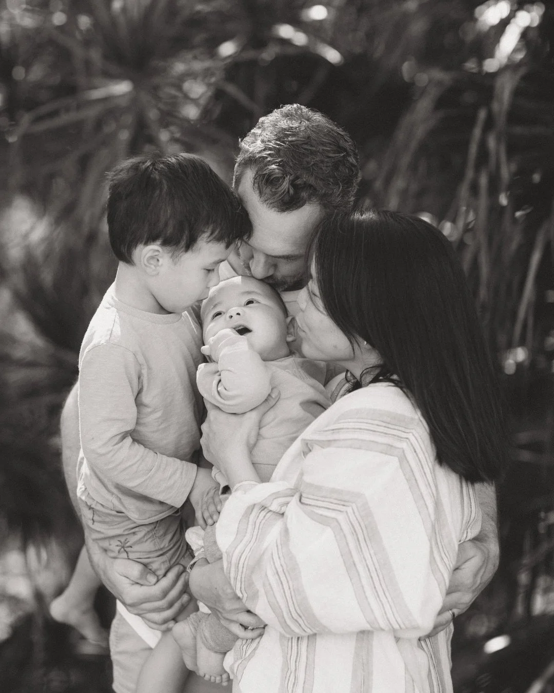 Black and white photo of family surrounding and cuddling newborn baby