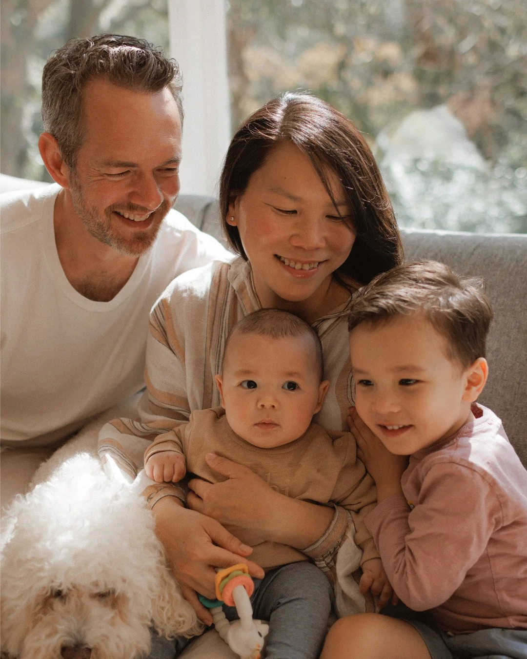 Family with baby and toddler sitting on couch with dog