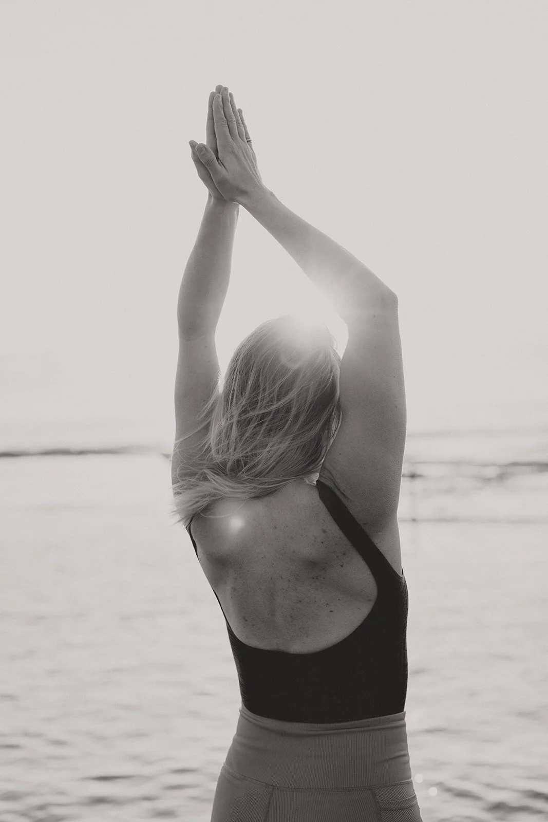 Woman standing by the ocean doing a yoga stretch at sunrise