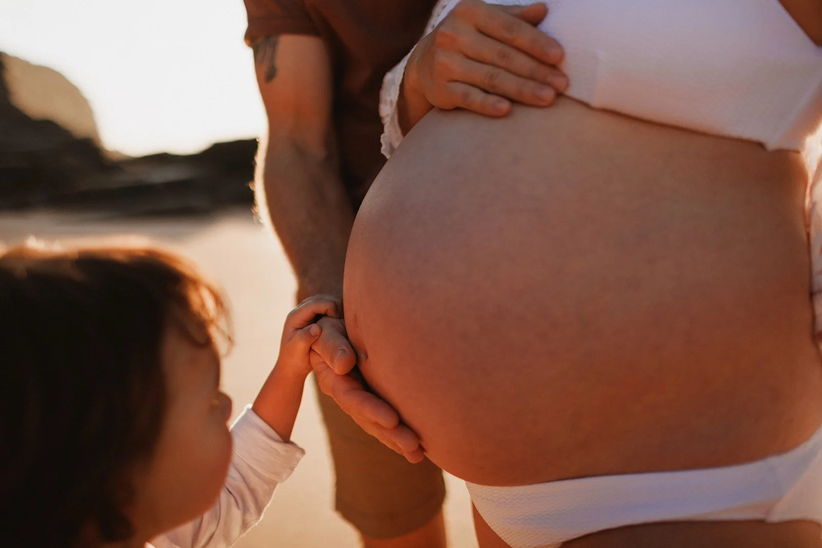 Pregnant woman with man and child's hands on her tummy, on the beach
