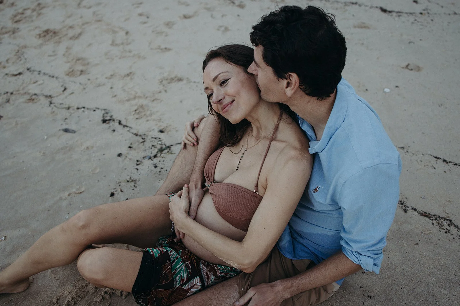 Pregnant woman cuddling partner on the beach