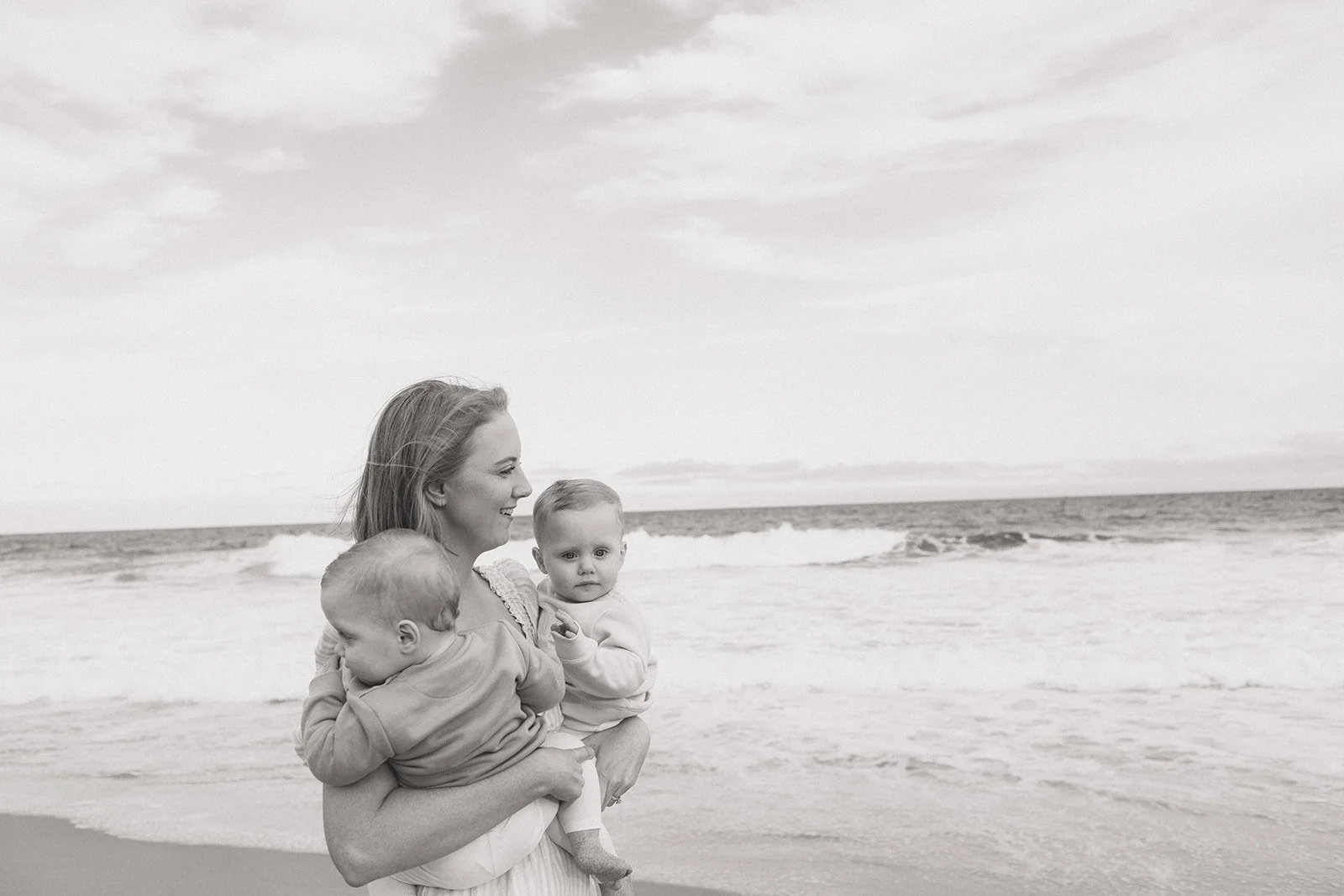 Mother cuddling twin boys on the beach