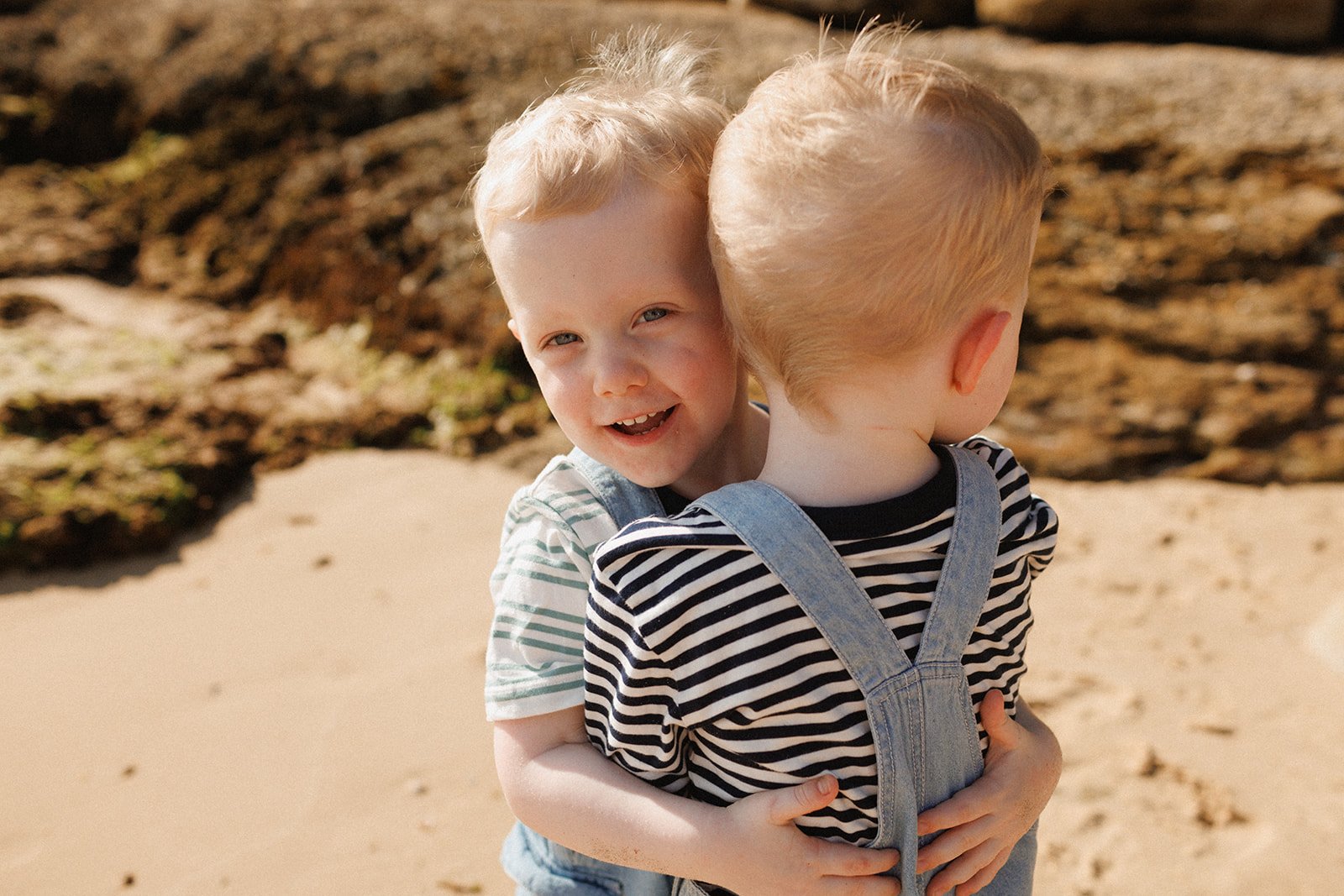 Twin toddler boys hugging on the beach